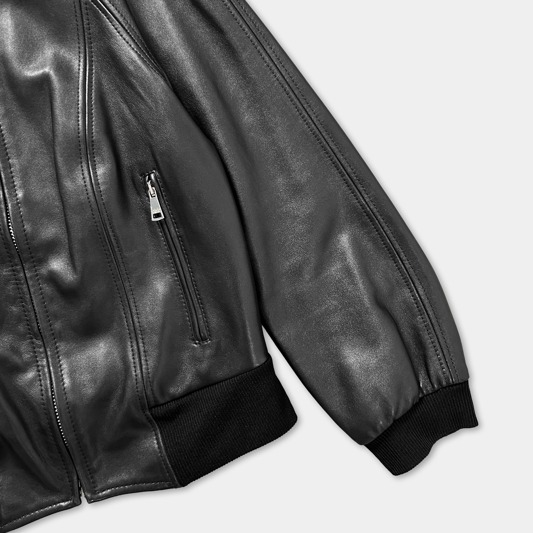 A close-up view of a black leather jacket with a zipper and a black fabric trim.