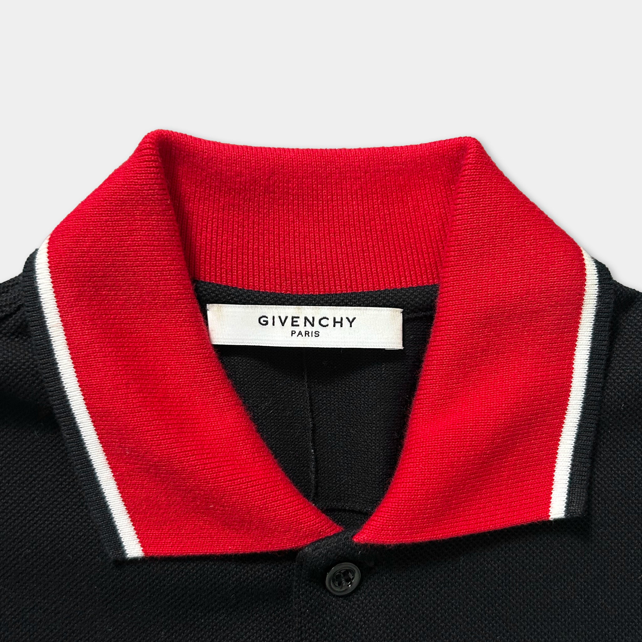 A close-up view of a collar and label on a polo shirt, with a red collar and a black and white label that reads "GIVENCHY PARIS".