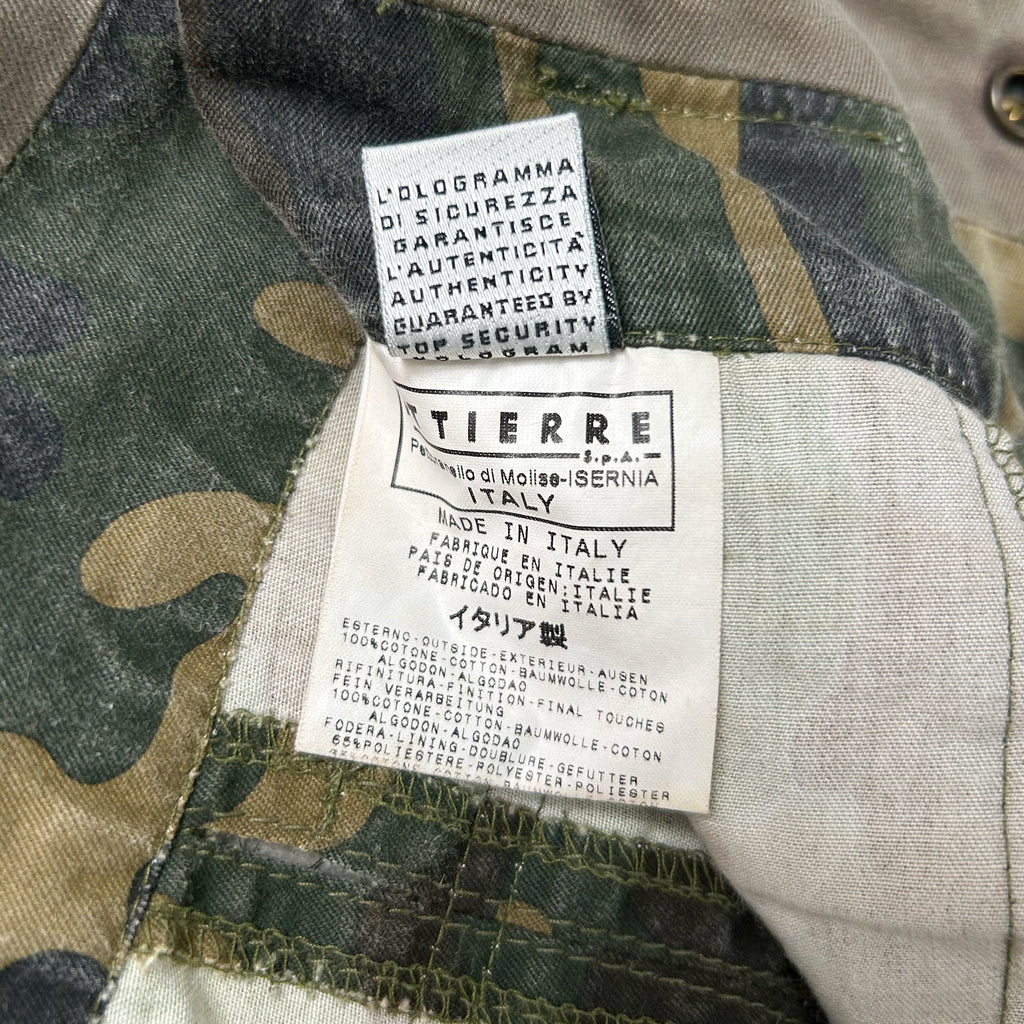 a close-up view of a label on a camouflage fabric, likely a military uniform, with text indicating the brand and product details.