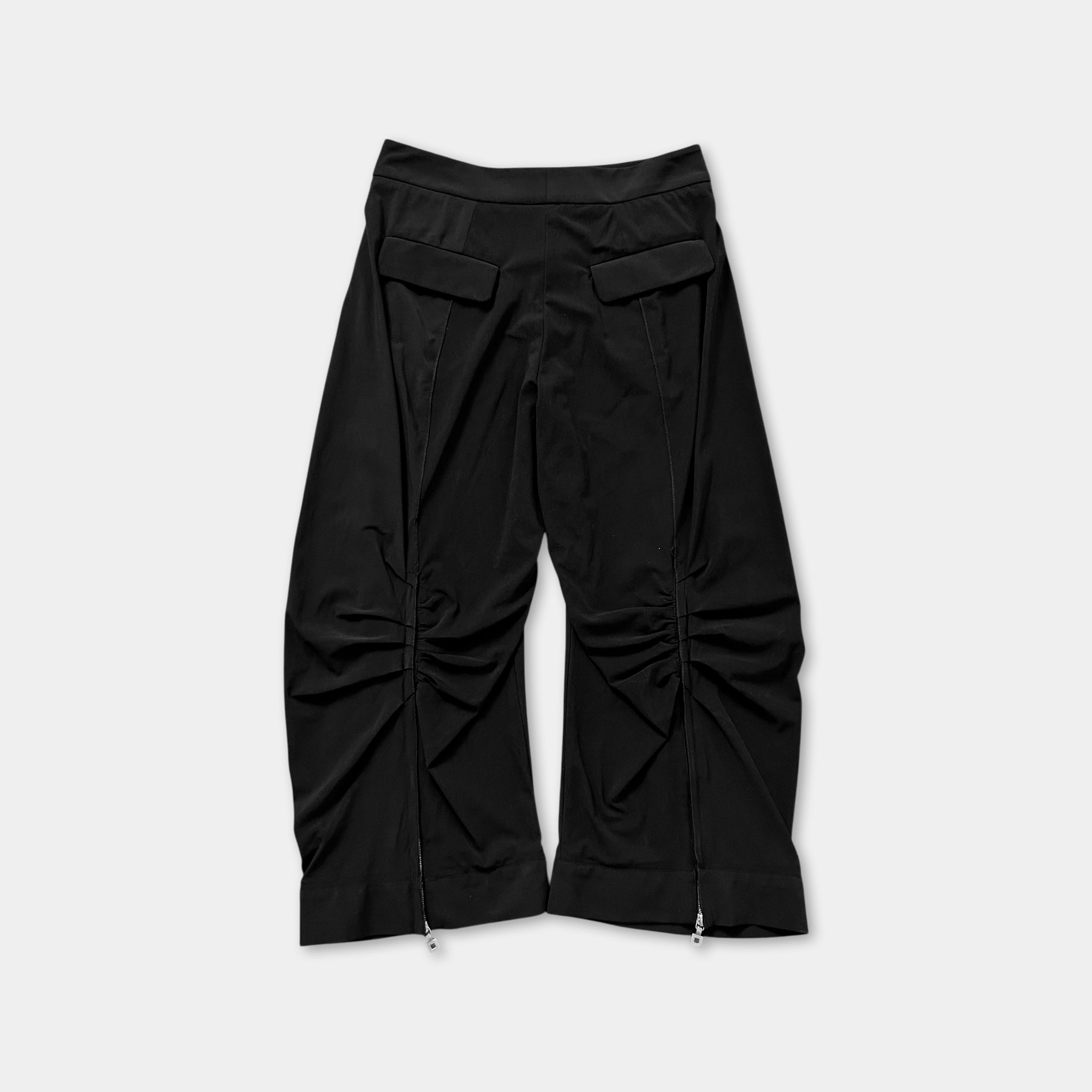 A pair of black pants with a ruched design and zippers on the sides.