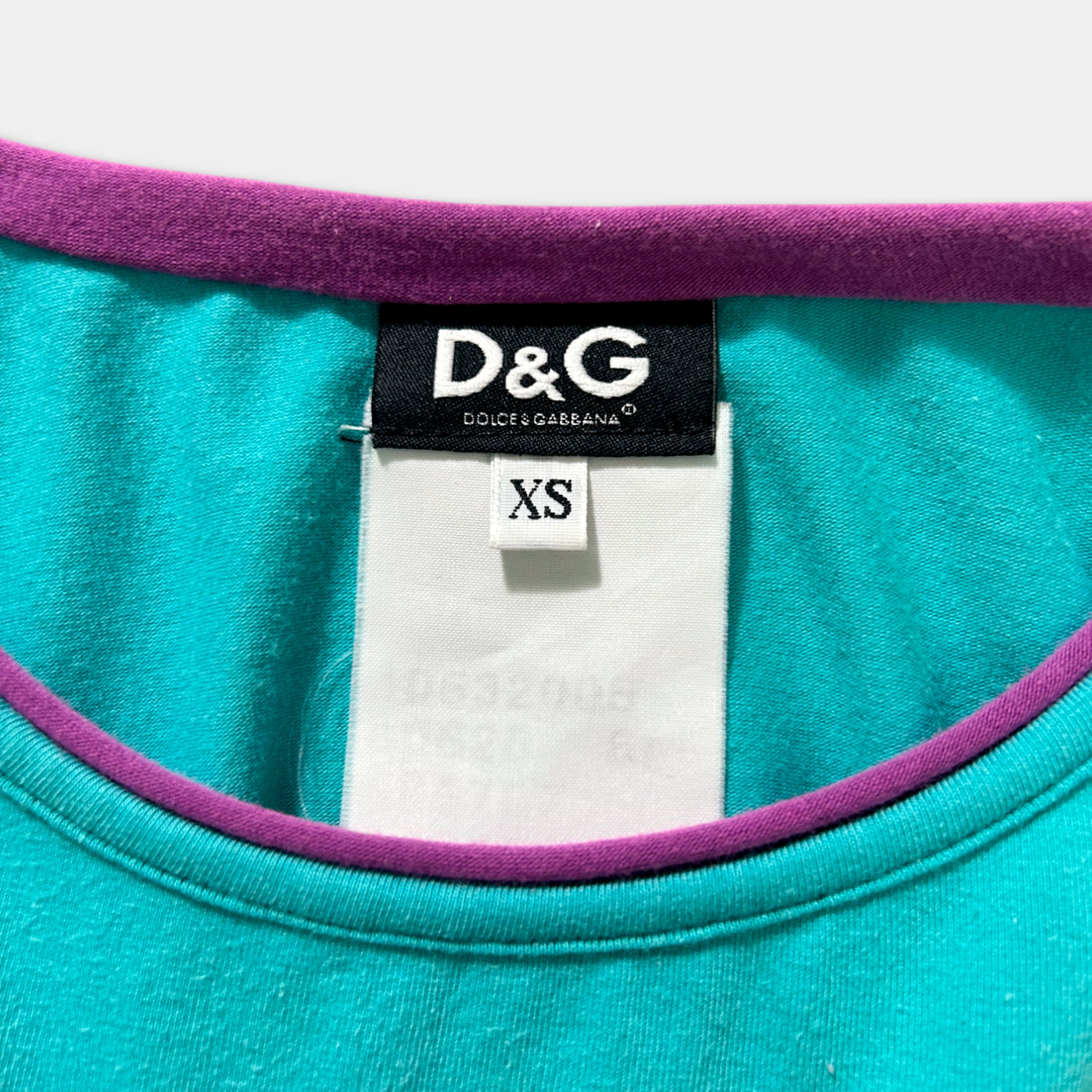 A close-up view of a teal-colored shirt with a purple collar, featuring a D&G (Dolce & Gabbana) label and a white tag with a size reference.