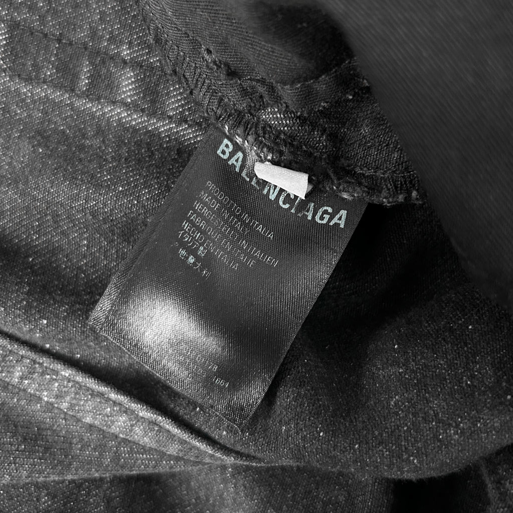 A close-up black and white image of a fabric label with text, likely from a clothing item.