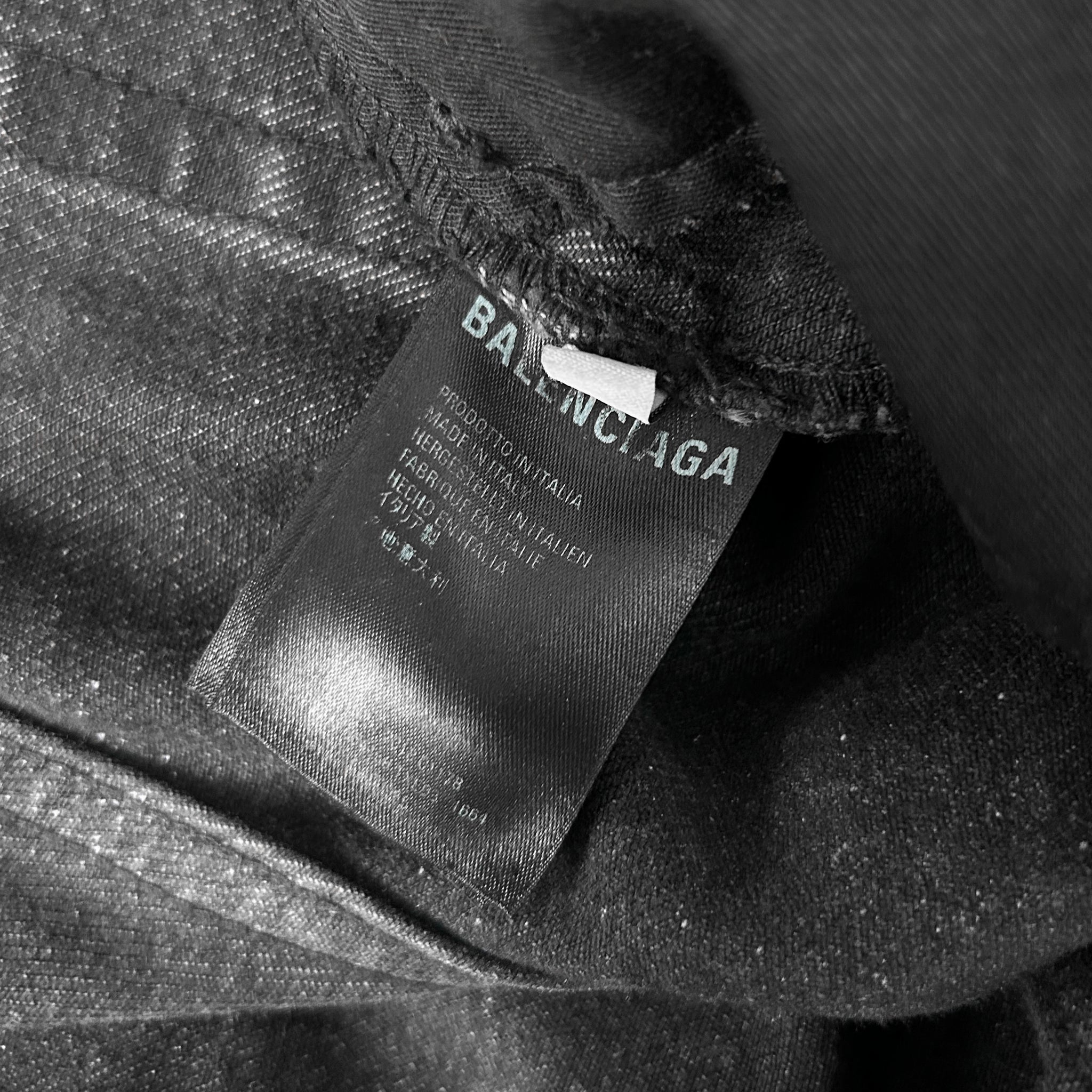 A close-up black and white image of a fabric label with text, likely from a clothing item.