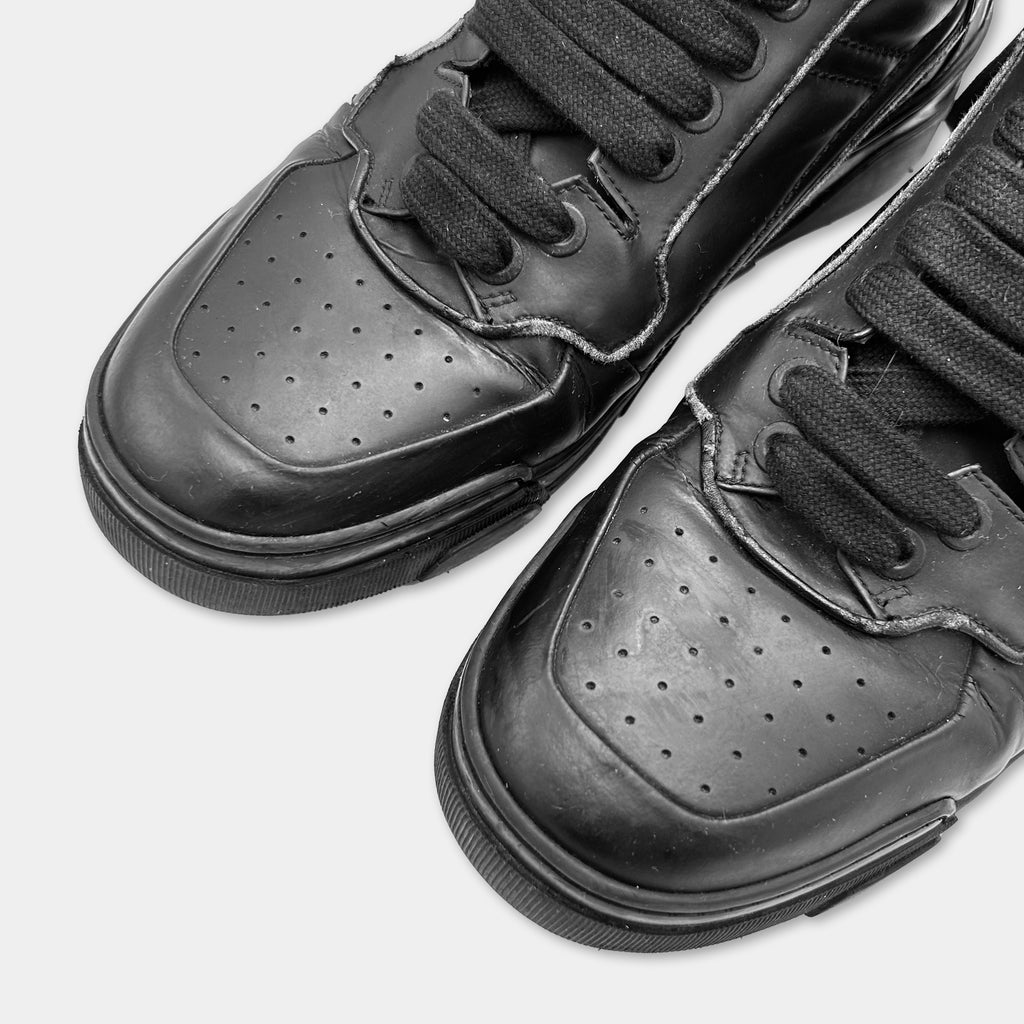 A close-up of a pair of black leather sneakers with a textured sole and laces.
