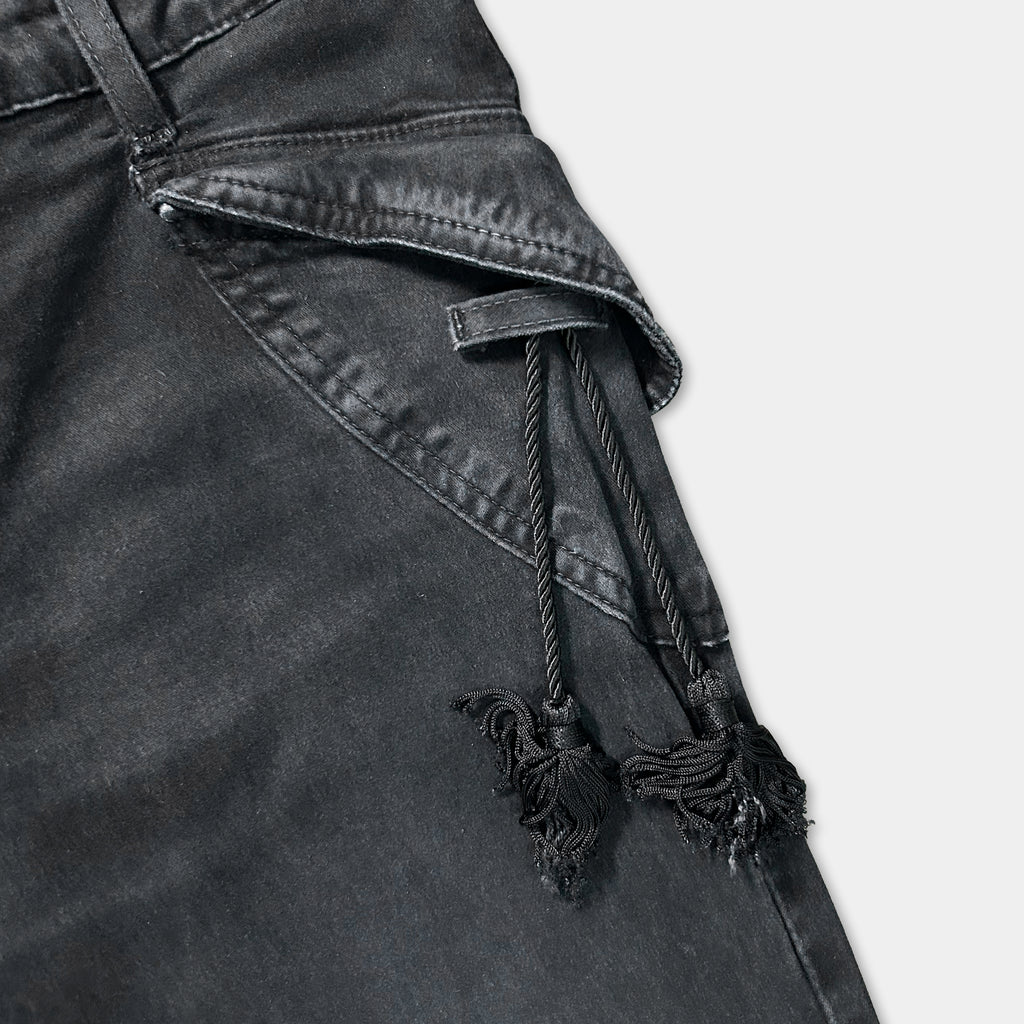 A close-up view of a pair of black jeans with a pocket and a tassel hanging from the pocket.
