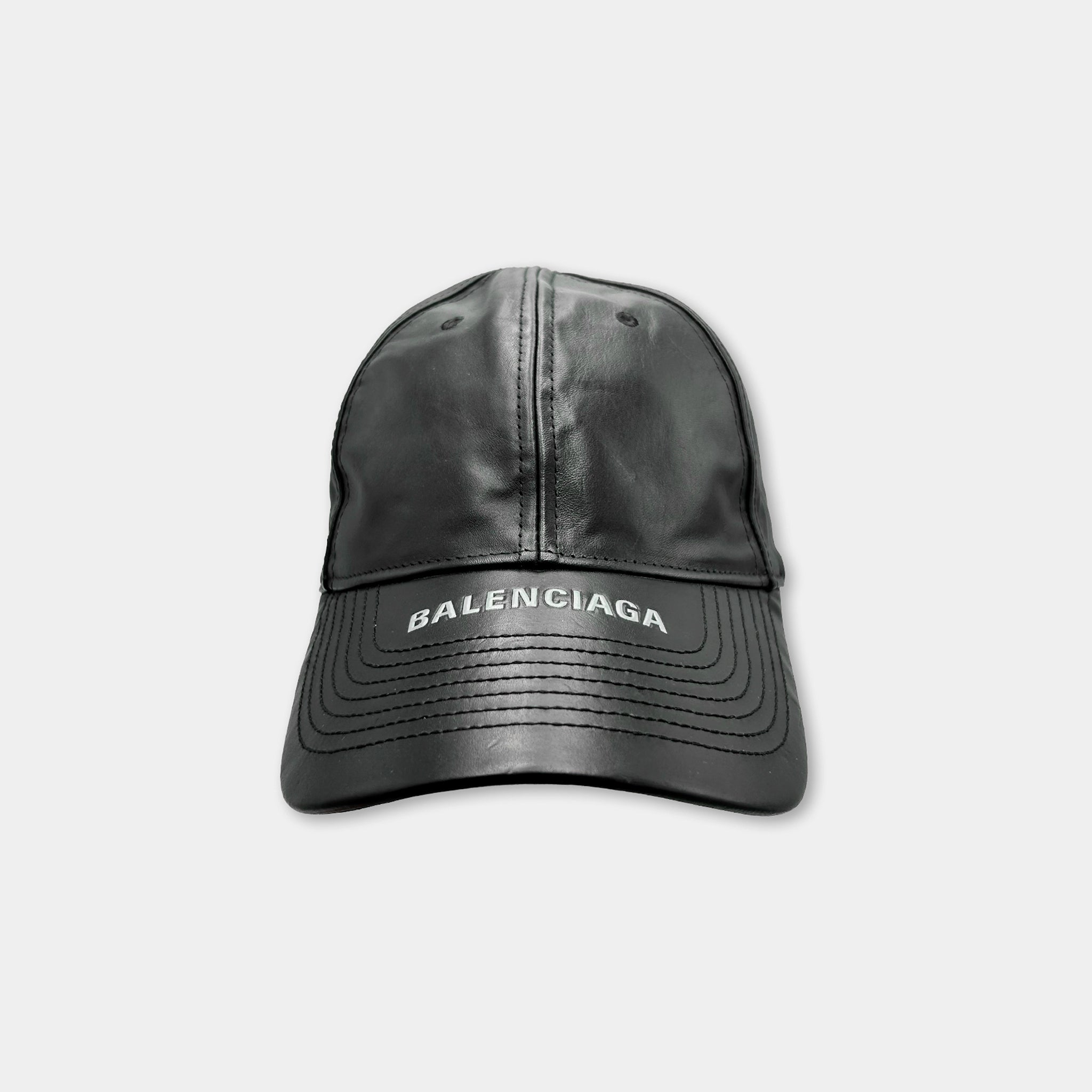 A black leather baseball cap with the Balenciaga logo printed on it.