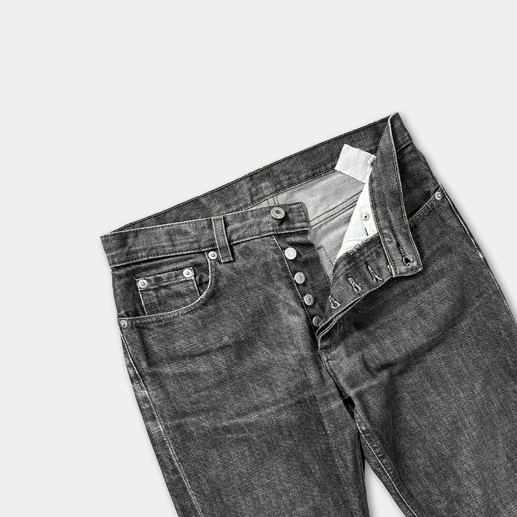 A pair of black jeans with a pocket and buttons is shown against a plain background.