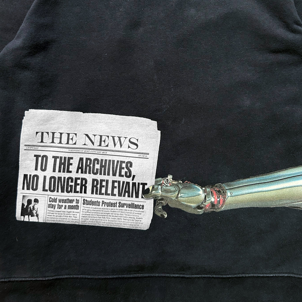 A black t-shirt with a printed newspaper headline and a metallic robotic arm.