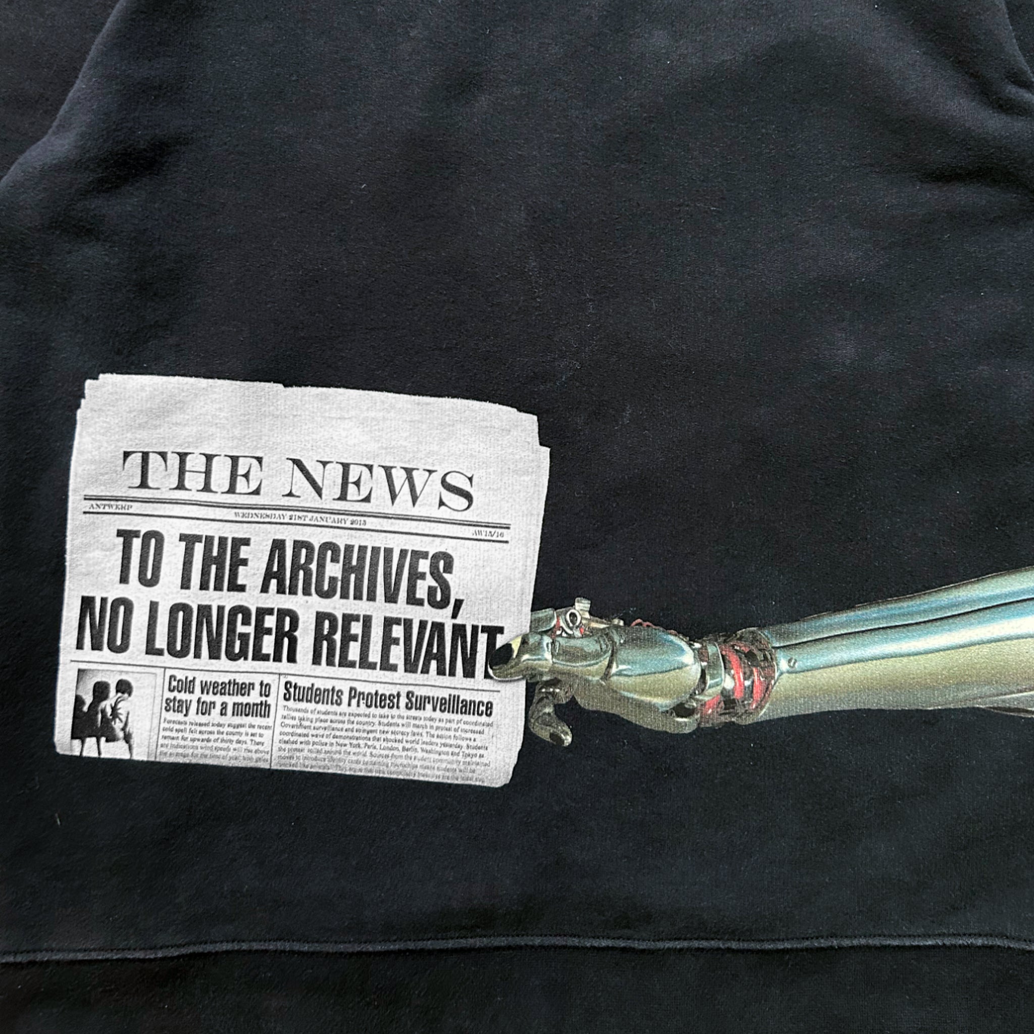 A black t-shirt with a printed newspaper headline and a metallic robotic arm.