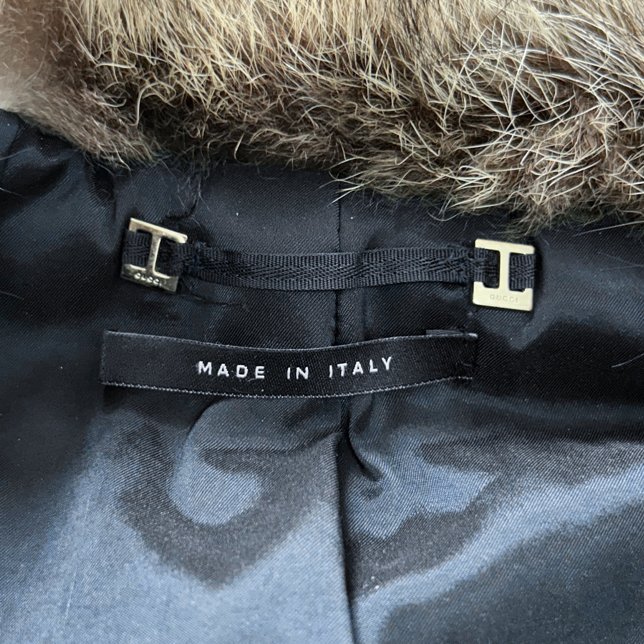 a close-up view of a black fabric with a fur collar and a label that reads "MADE IN ITALY".