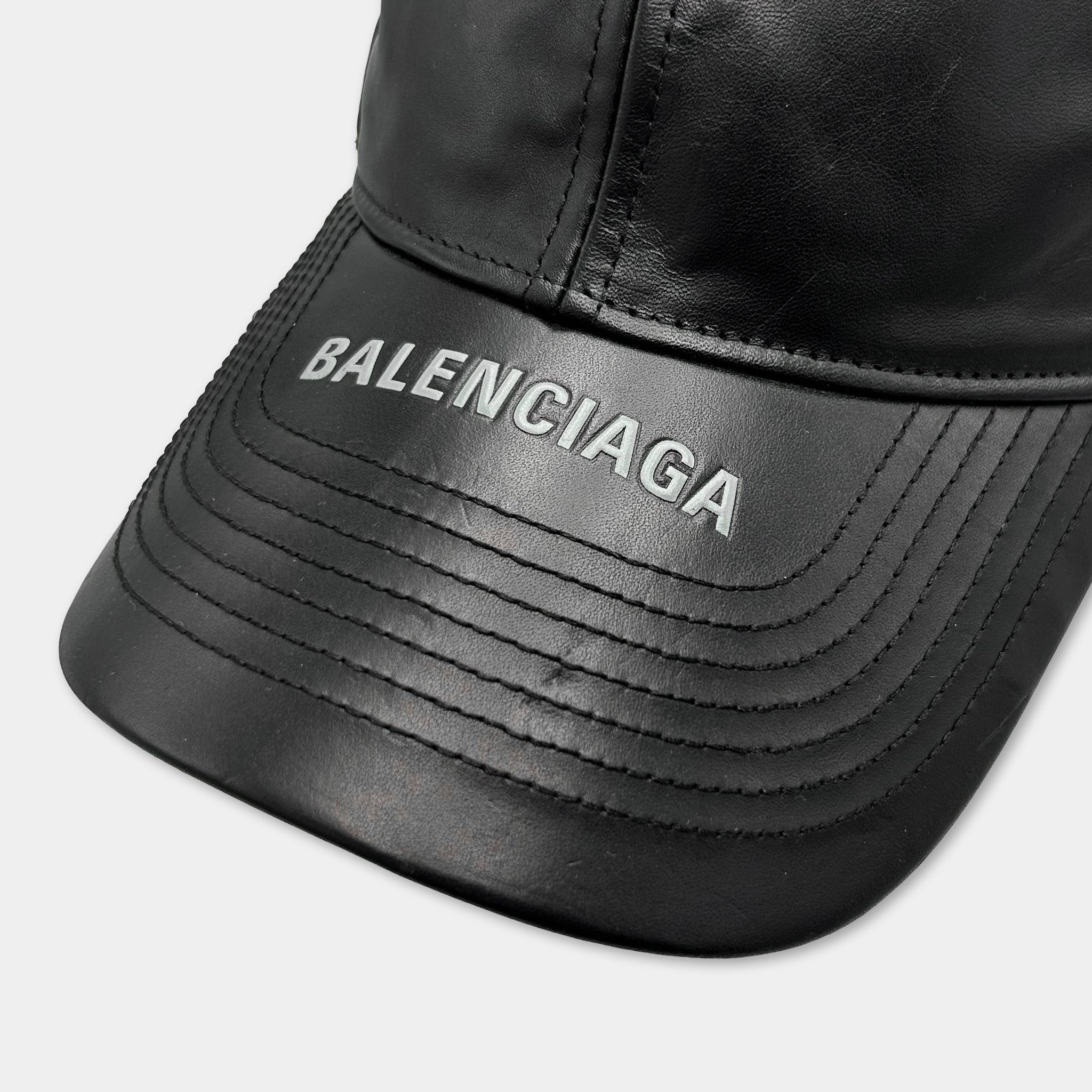 A close-up view of a black leather baseball cap with the word "BALENCIAGA" printed on it.