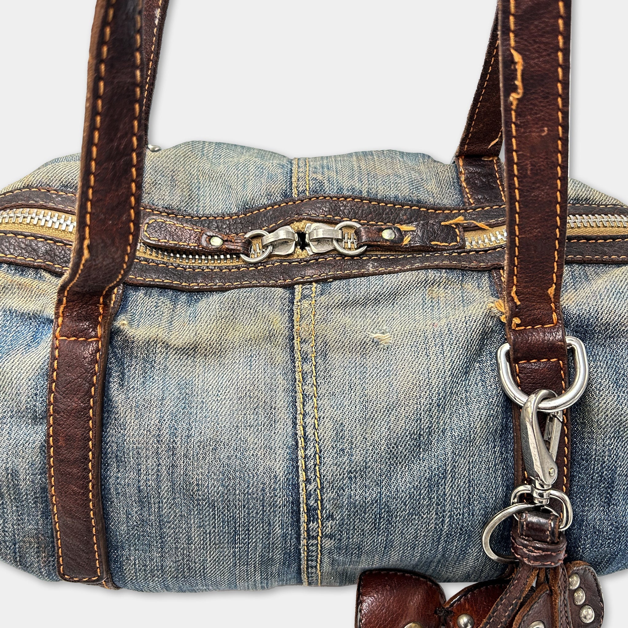 A close-up view of a handbag made from a denim fabric, with leather straps and zippers.