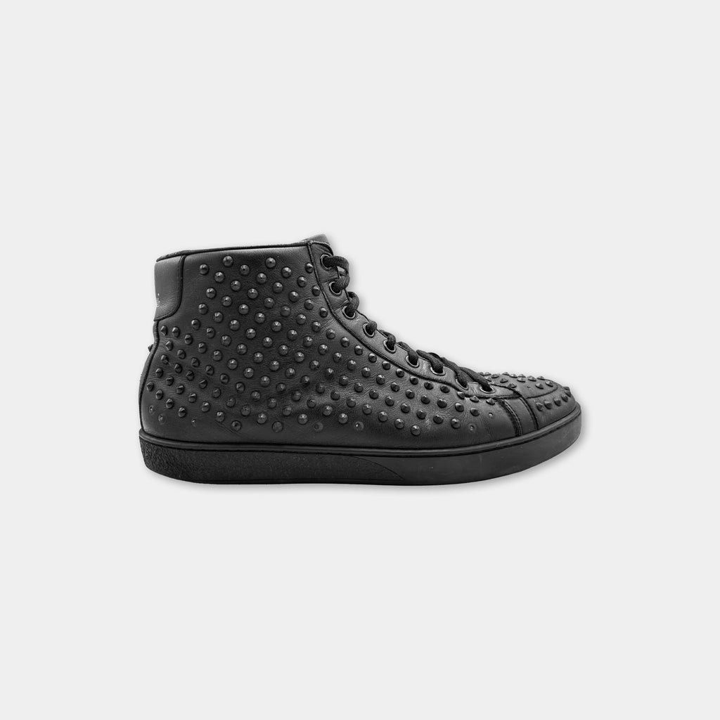 A black high-top sneaker with a studded sole and laces.