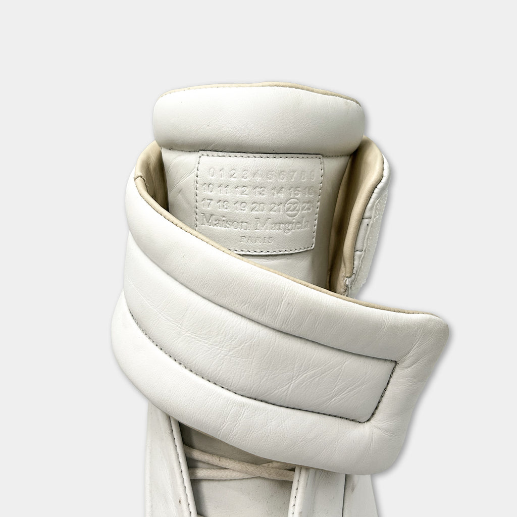 A close-up view of a white leather shoe, showing the brand name and logo on the heel.