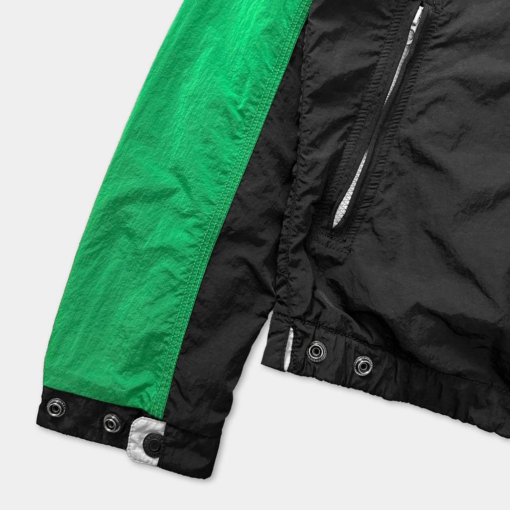 a close-up view of a jacket with a green and black color scheme. The jacket has a zipper and buttons, and it appears to be made of a shiny, textured material.