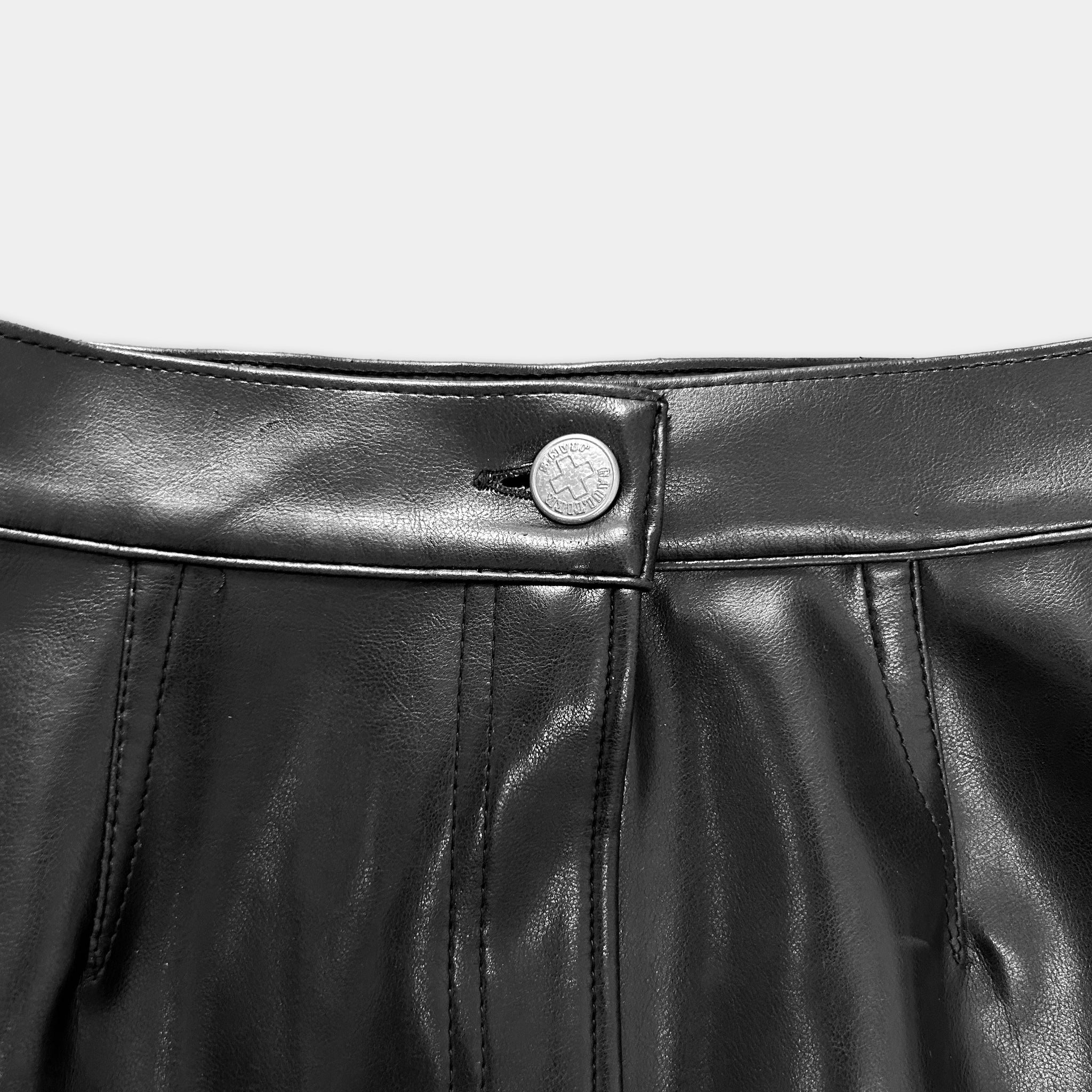 A close-up view of a black leather skirt, focusing on the waistband and a button.