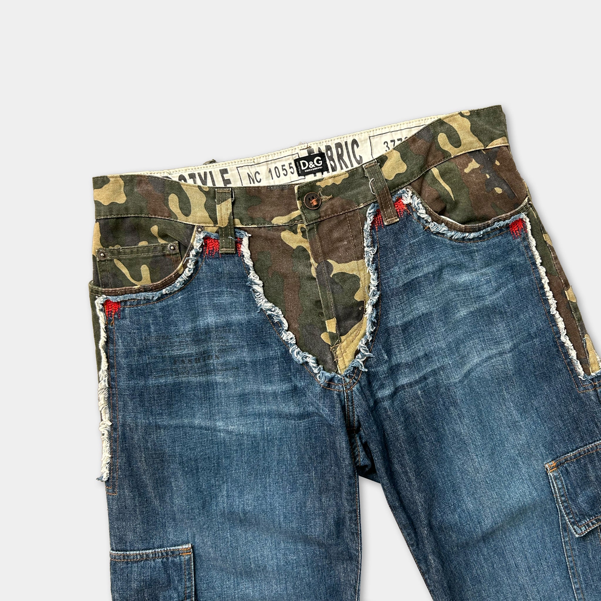 A pair of camouflage-patterned jeans with frayed edges and red stitching on the pockets.
