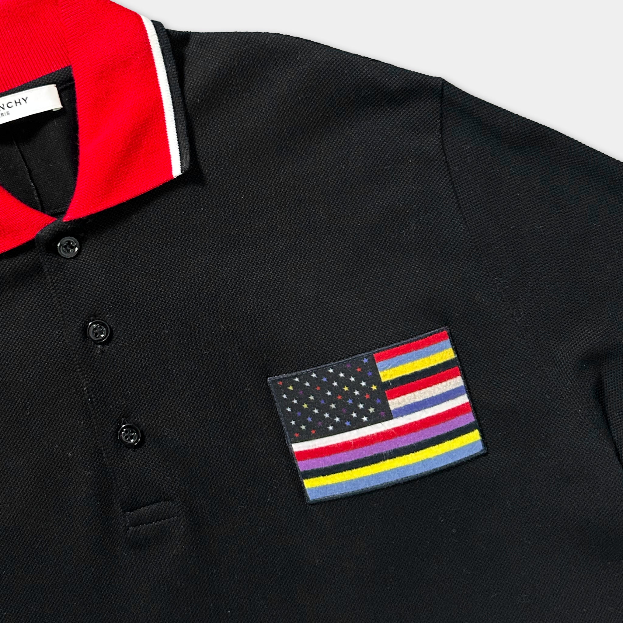 a black polo shirt with a red collar and a small American flag patch on the front.