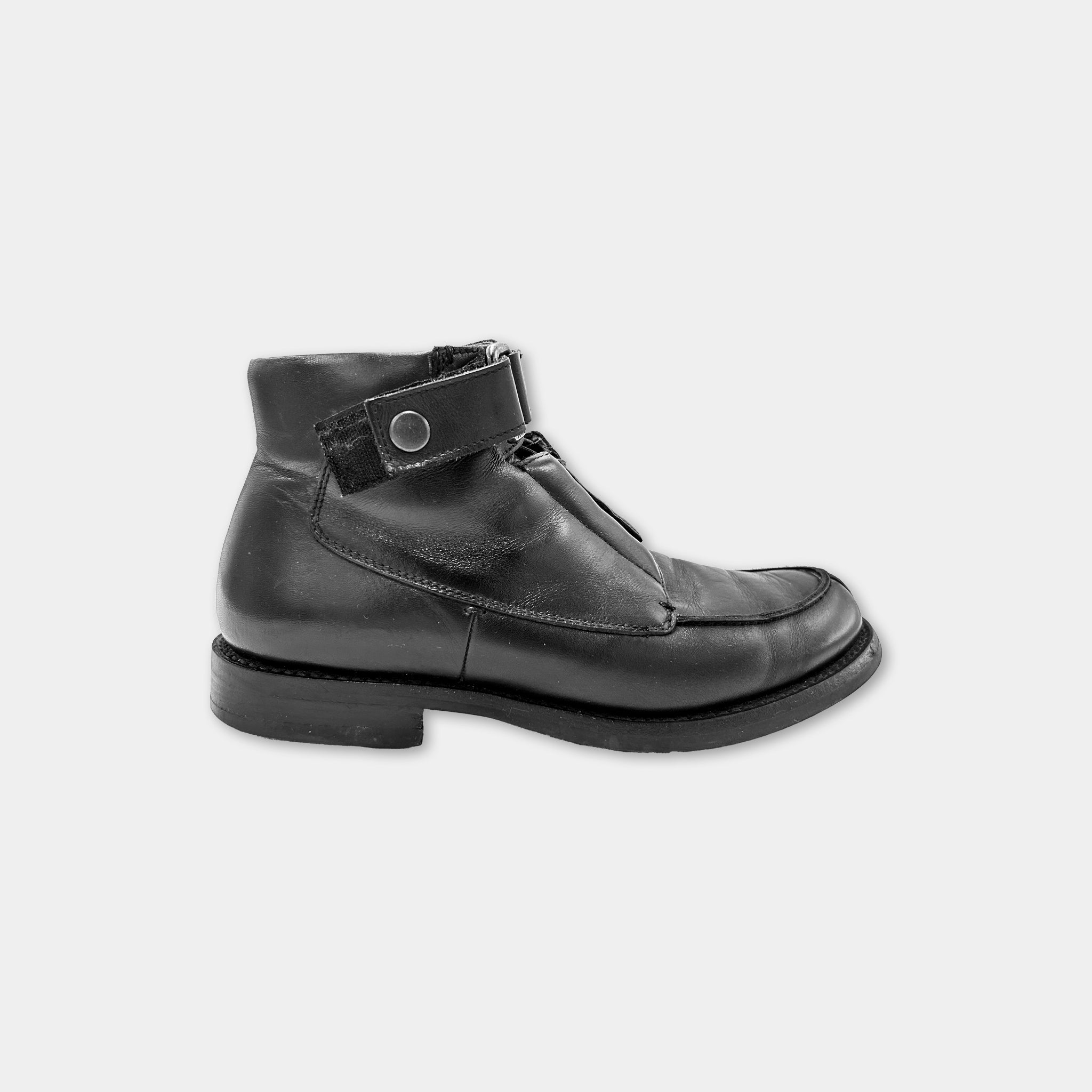 A black leather boot with a zipper detail and a round buckle on the side.