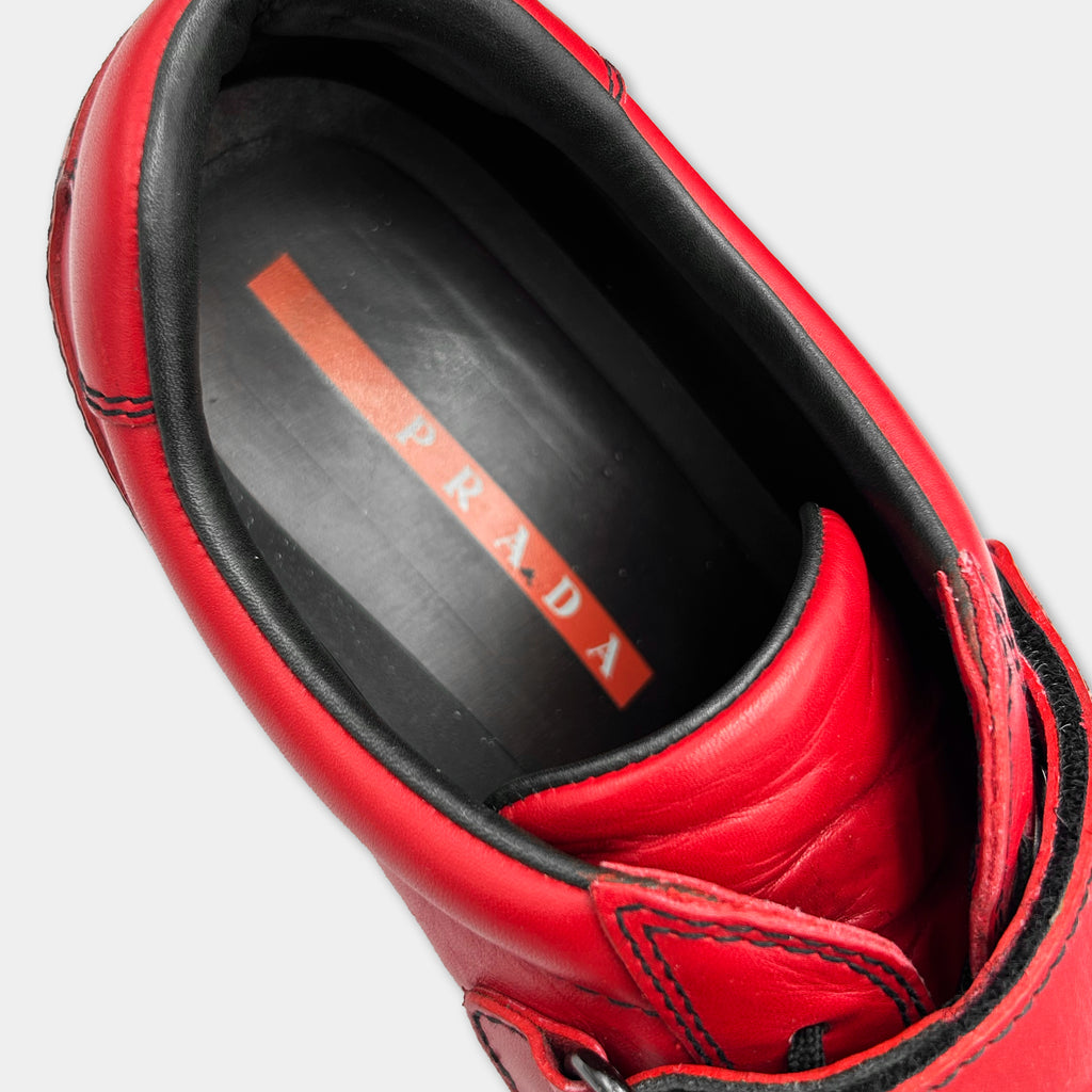A close-up view of a red Prada shoe, showing the brand name on the sole.