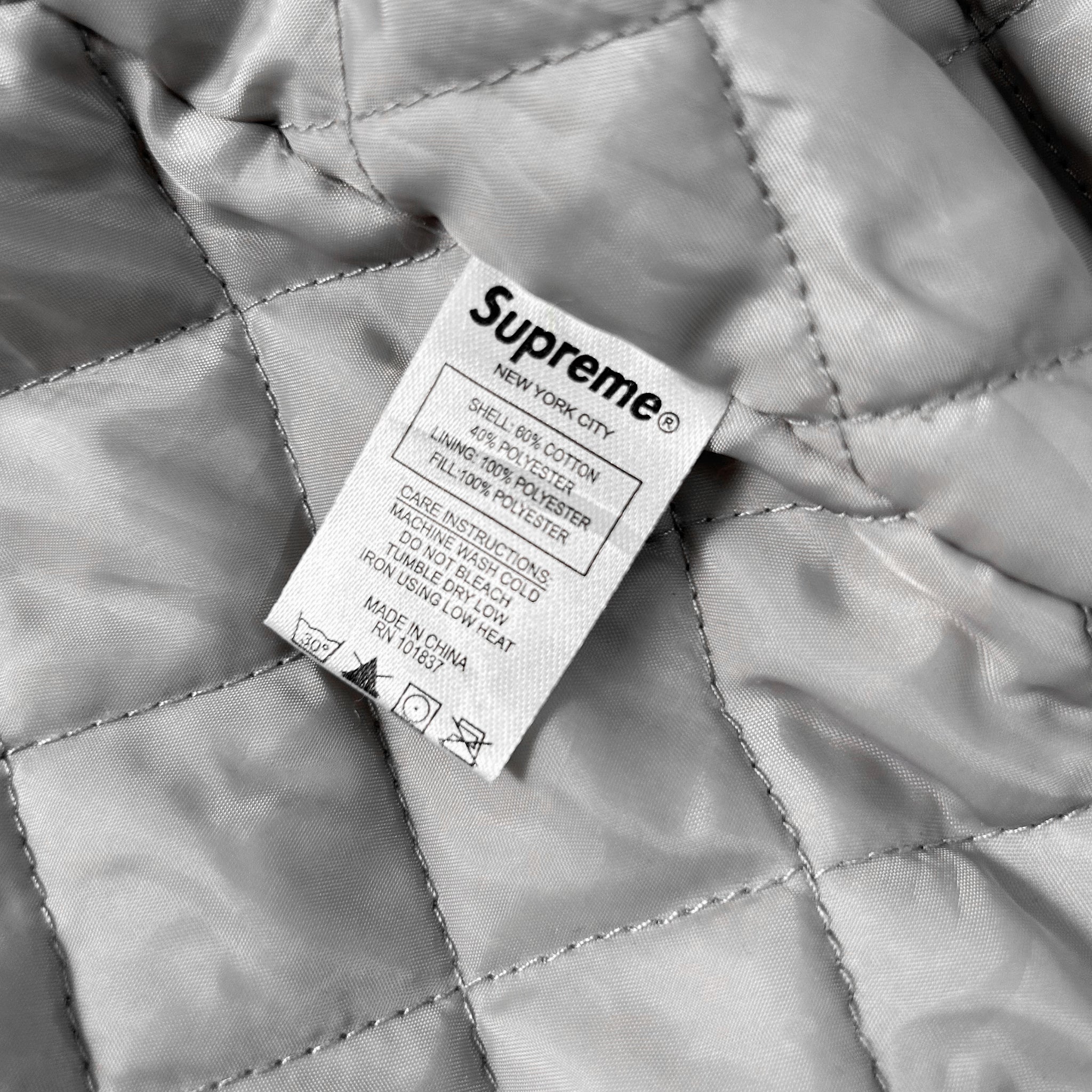 A close-up view of a white label with text on a grey fabric, likely a quilted material.