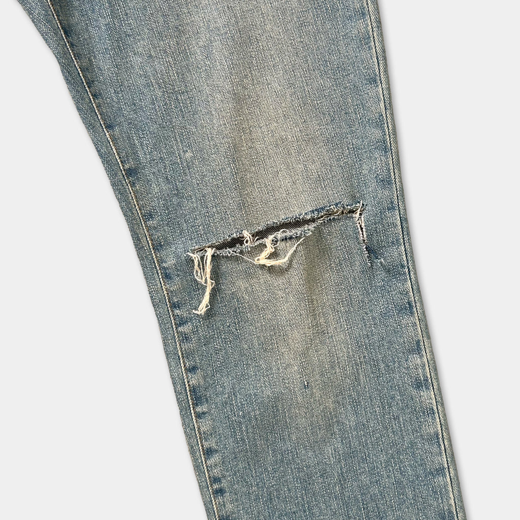 A close-up view of a pair of blue jeans with a noticeable tear in the knee area.