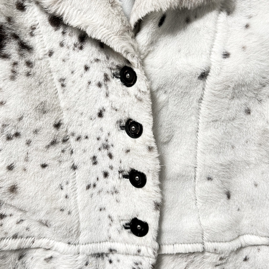 A close-up view of a white fur coat with black spots, showing the buttons and collar.