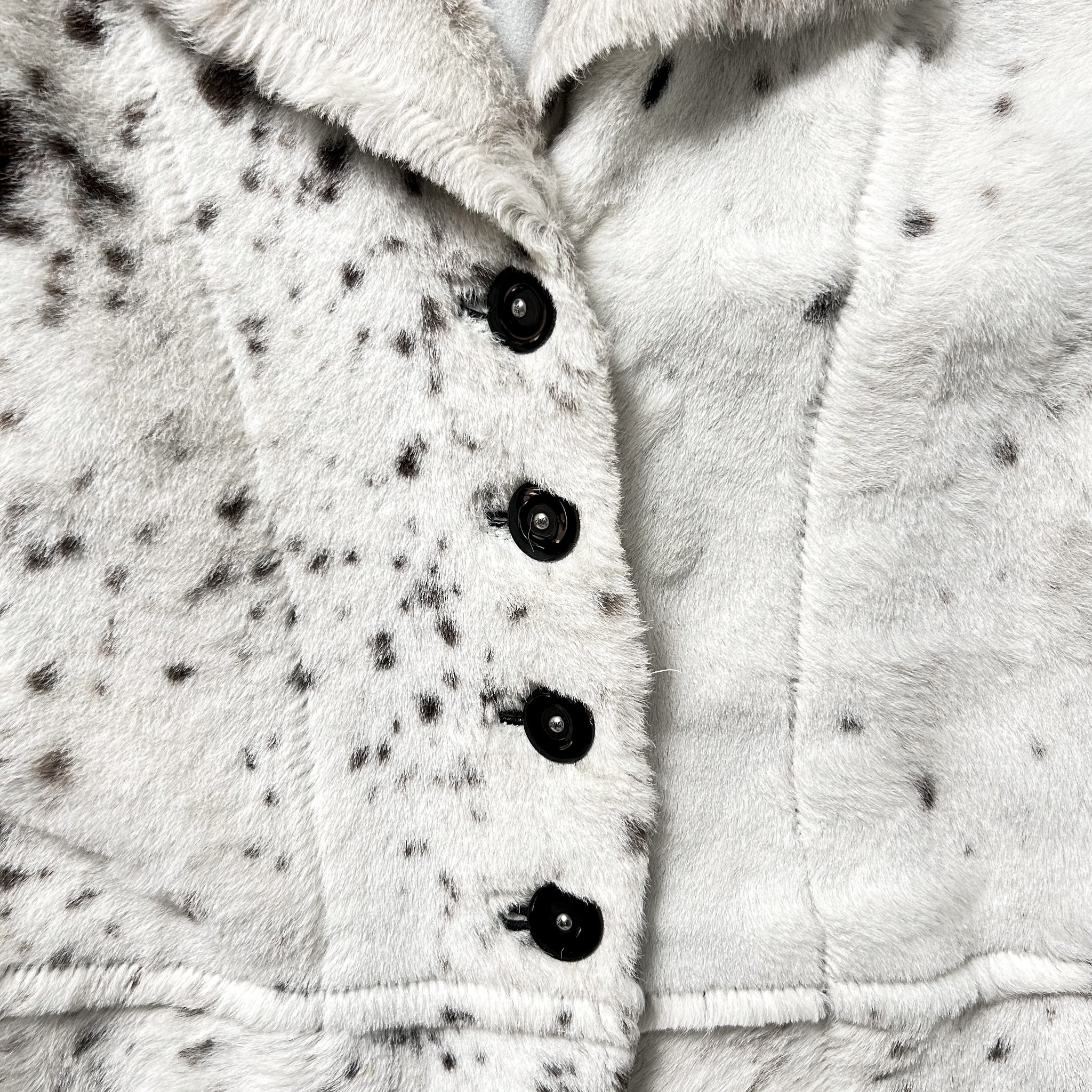 A close-up view of a white fur coat with black spots, showing the buttons and collar.