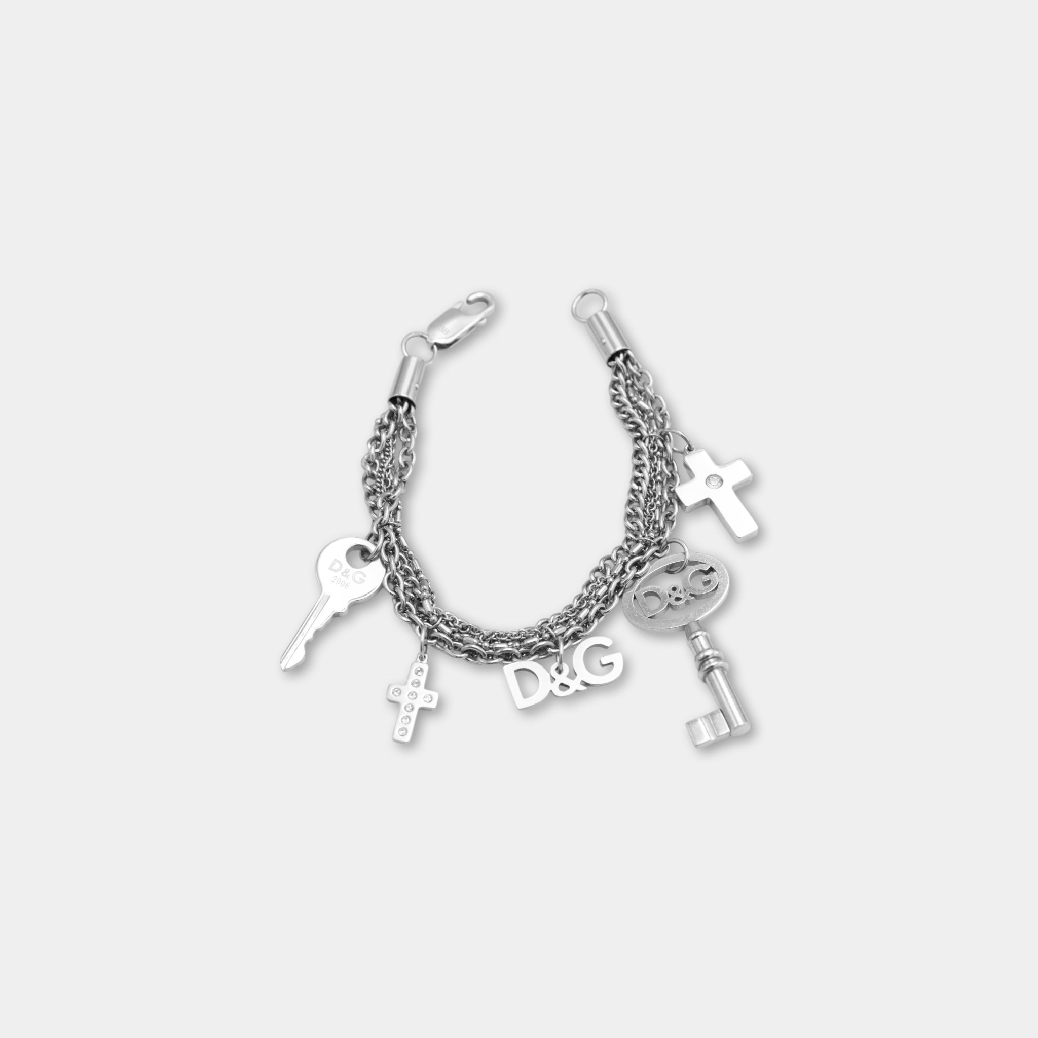 A silver-colored bracelet with various charms attached to it, including a cross, keys, and the letters 'D&G'.