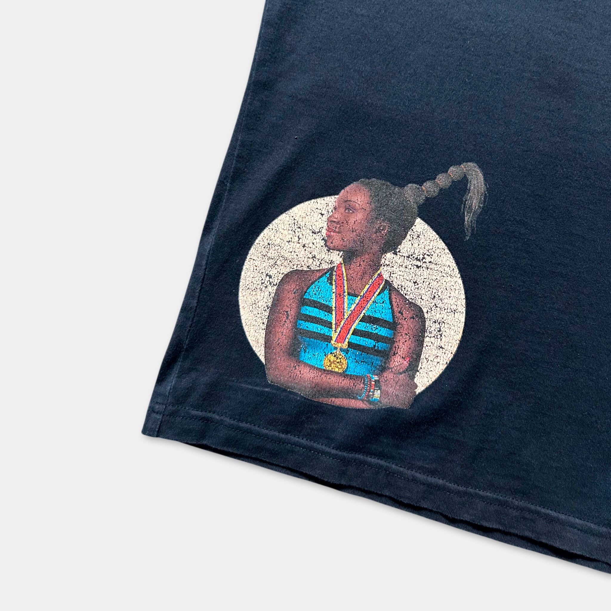 a black t-shirt with a graphic design depicting a woman wearing a blue and white striped top, holding a medal.