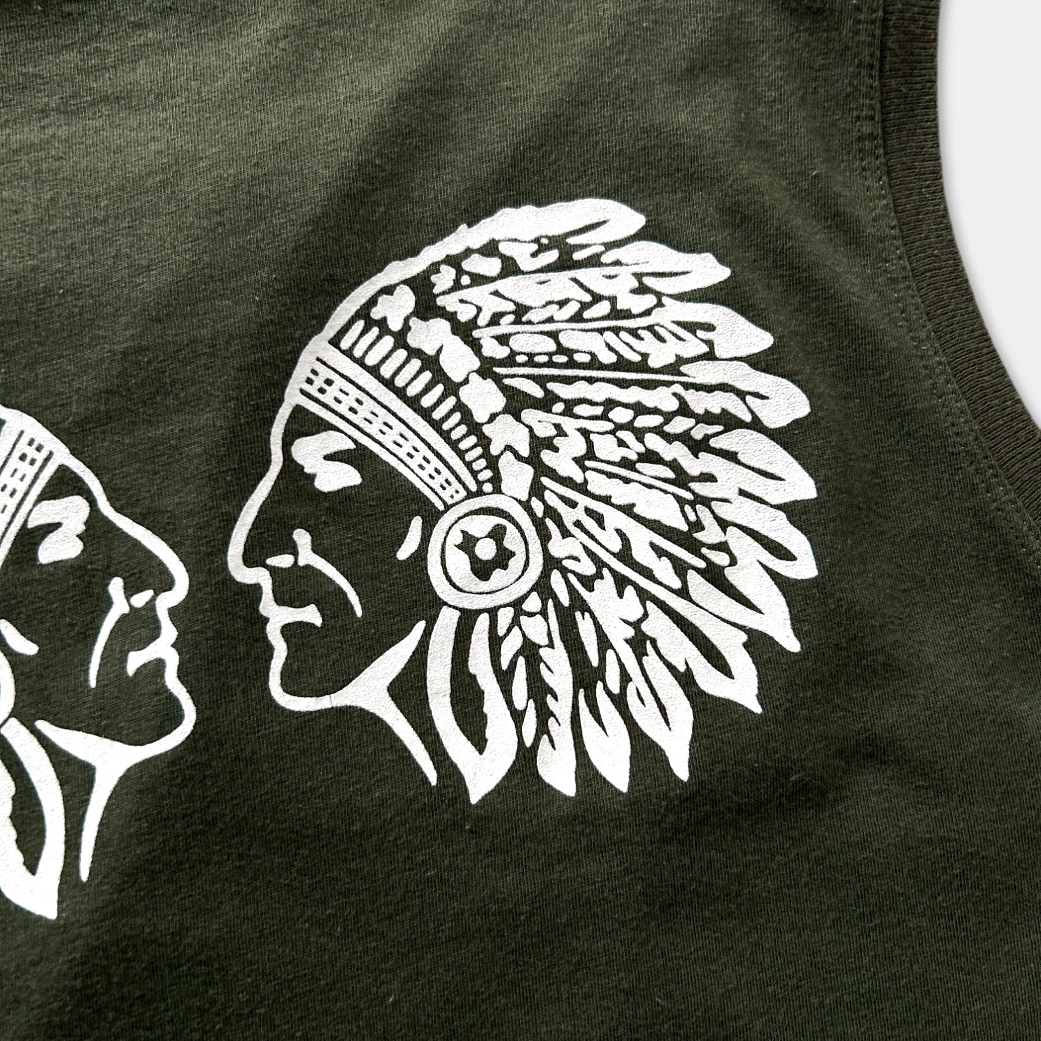 a close-up view of a dark green fabric with a white graphic design depicting the profile of a Native American headdress.