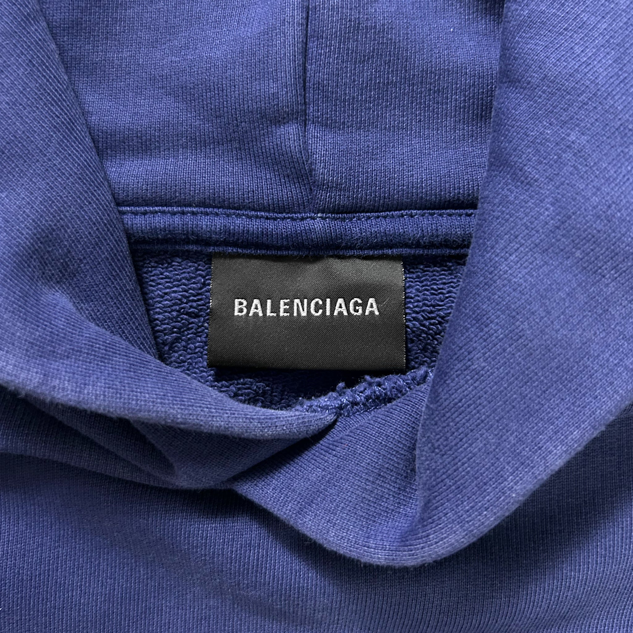 A close-up view of a blue fabric, possibly a sweater or hoodie, with a black label that reads "BALENCIAGA" prominently displayed.