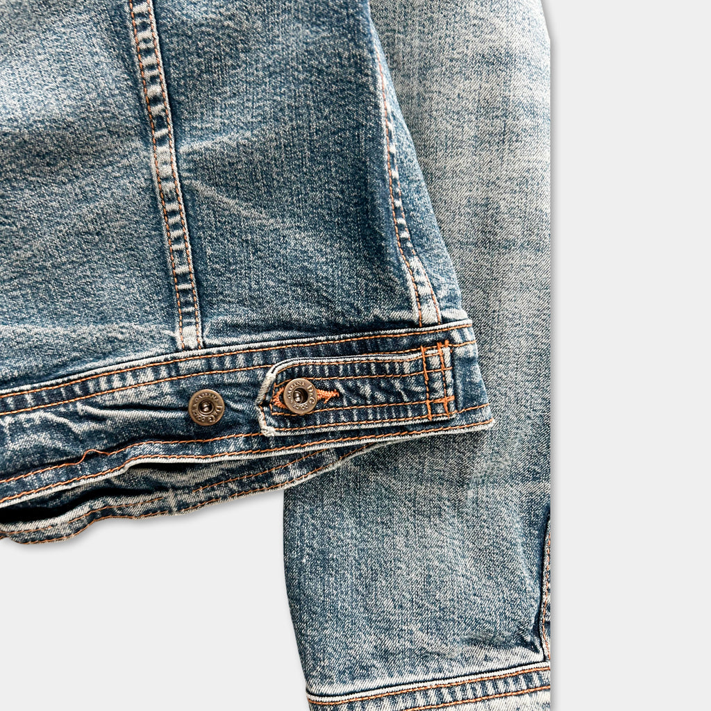 A close-up view of a pair of blue denim jeans, focusing on the zipper and belt detail.