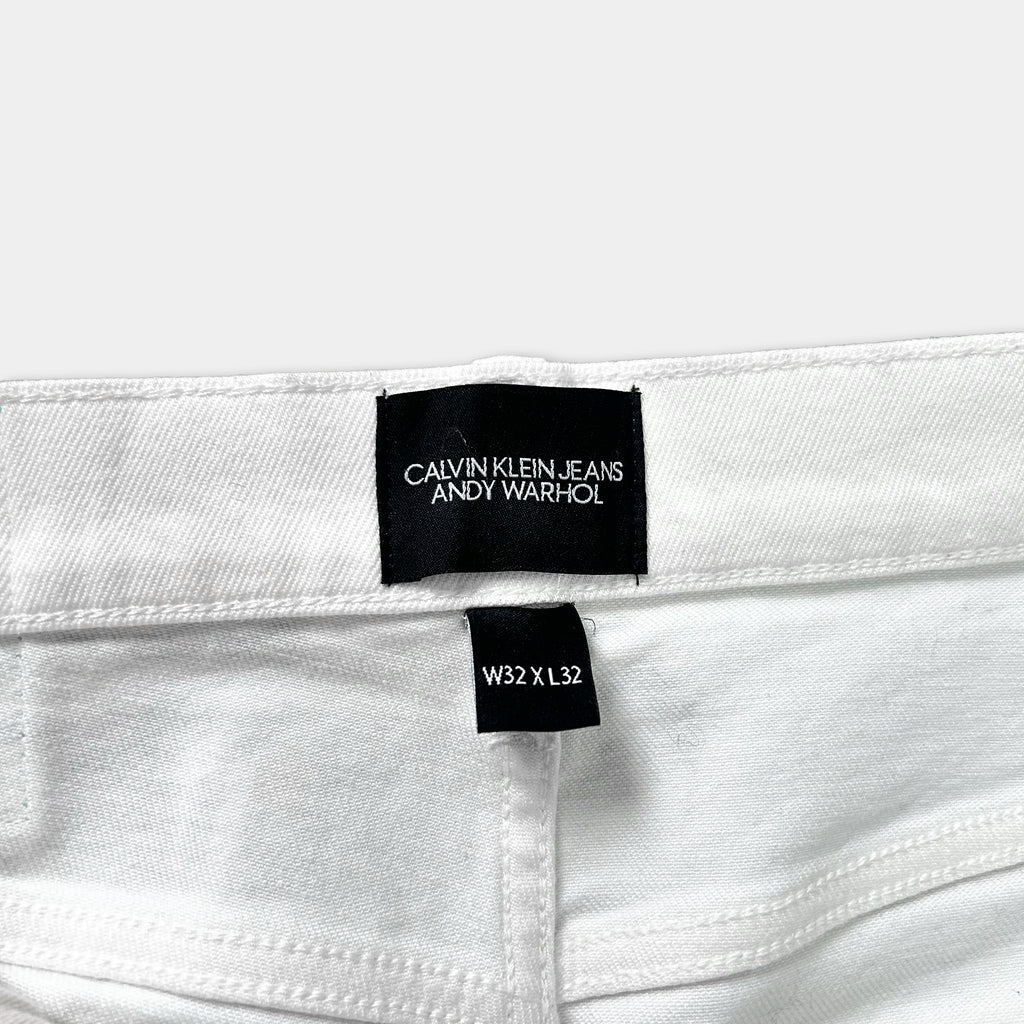 A close-up view of a white pair of Calvin Klein Jeans, showing the waistband and a label indicating the brand and size.