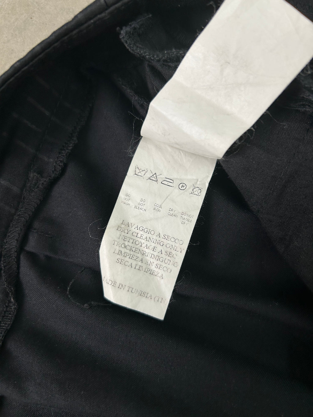 a close-up view of a black fabric, possibly a piece of clothing, with a white label attached to it. The label appears to contain text and symbols, but the image does not contain any text that can be transcribed.
