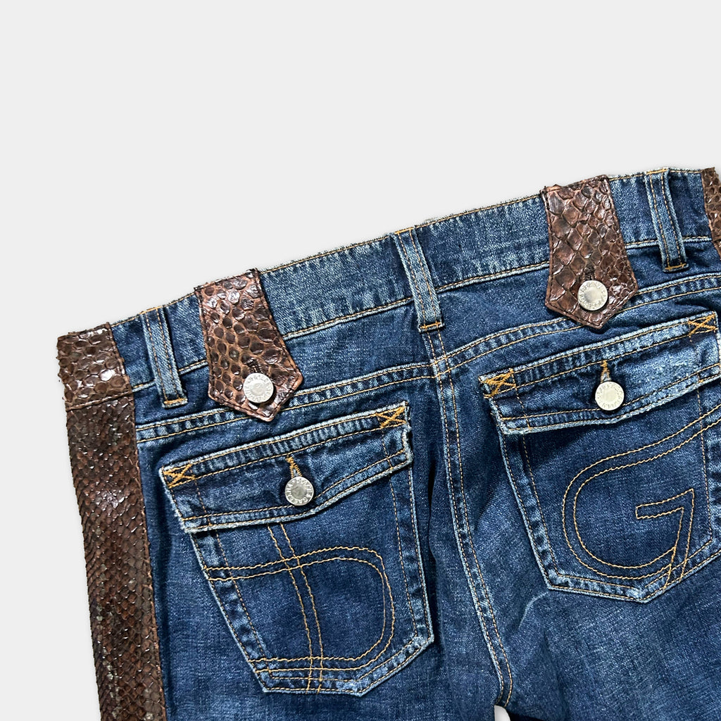 A pair of blue jeans with a brown leather belt and a snake skin-like pattern on the belt loops.