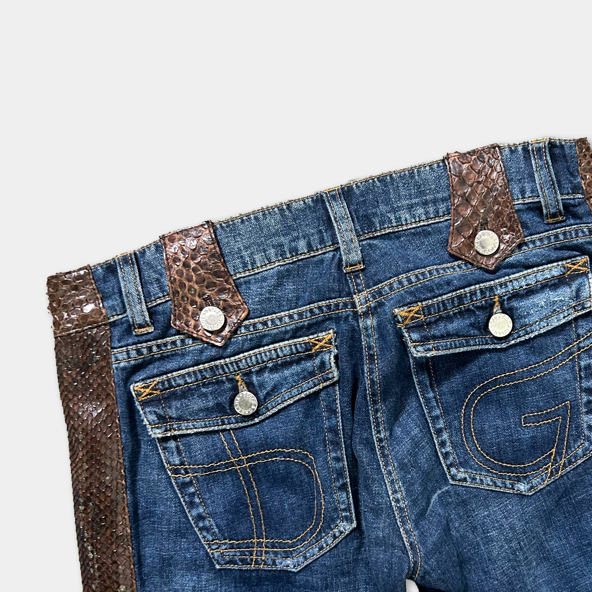 A pair of blue jeans with a brown leather belt and a snake skin-like pattern on the belt loops.