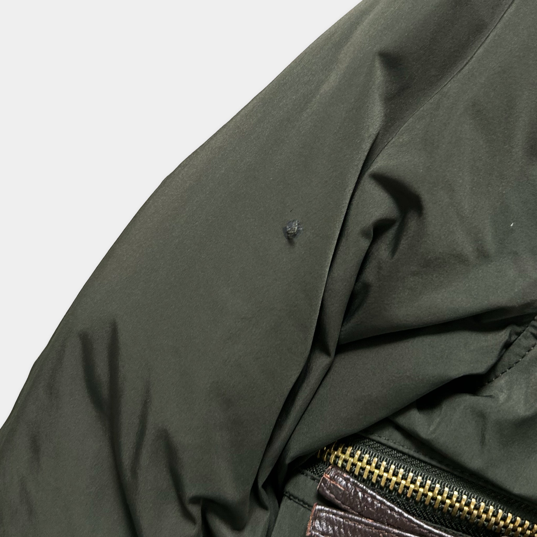 A close-up view of a dark green jacket with a small tear in the fabric.
