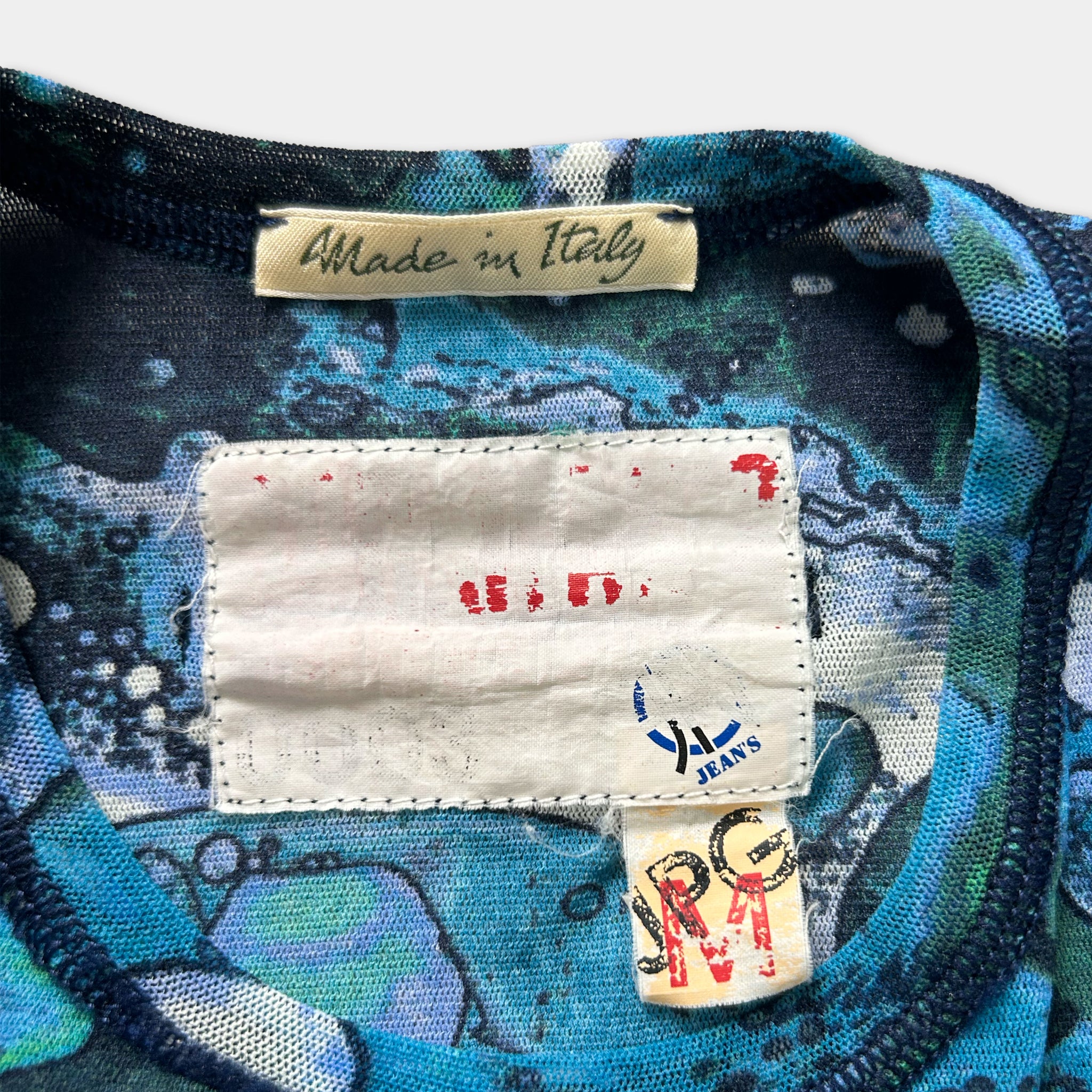 a close-up view of a colorful patterned fabric, possibly a shirt or garment, with a label attached to it. The label appears to be a handmade tag, indicating that the item was made in Italy.