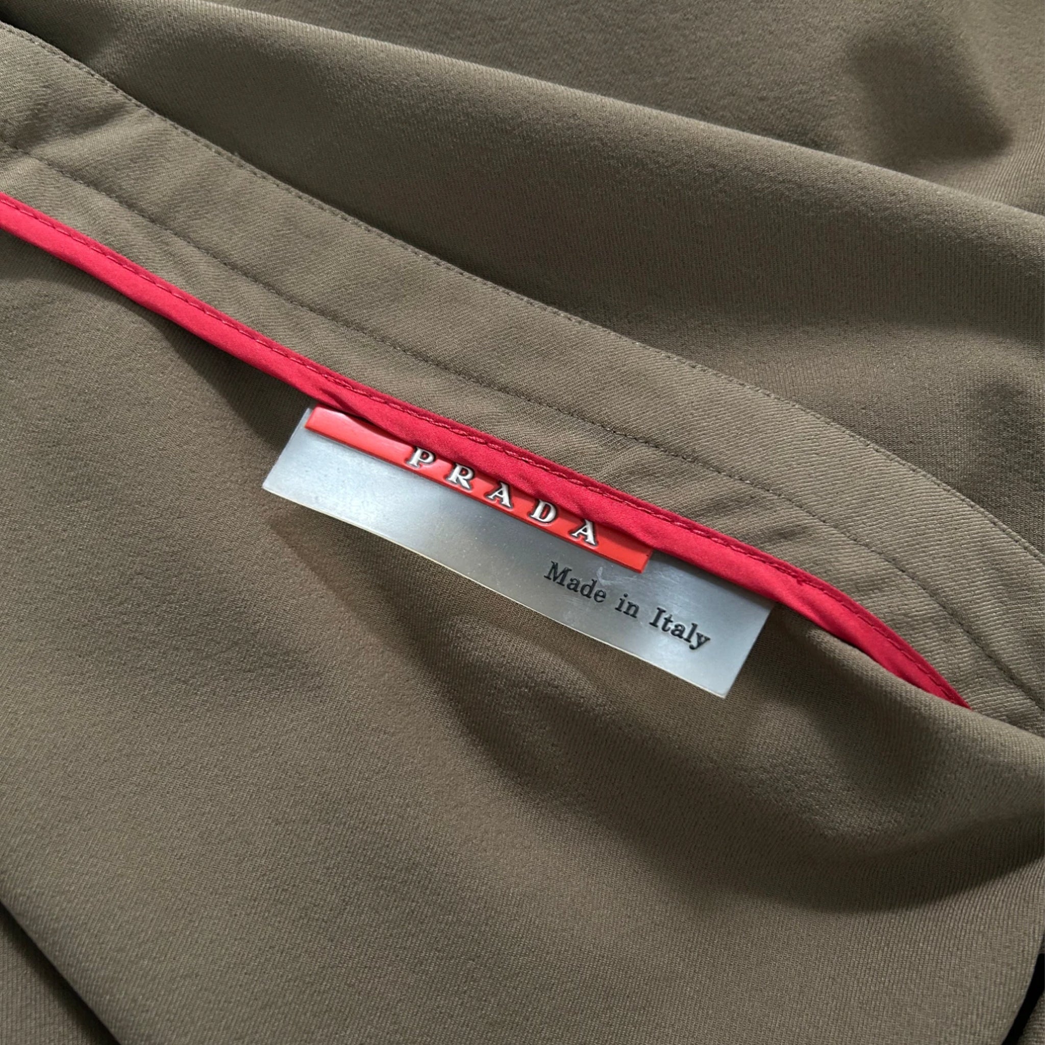 A close-up view of a Prada label on a piece of clothing, with a red tag attached to the label.