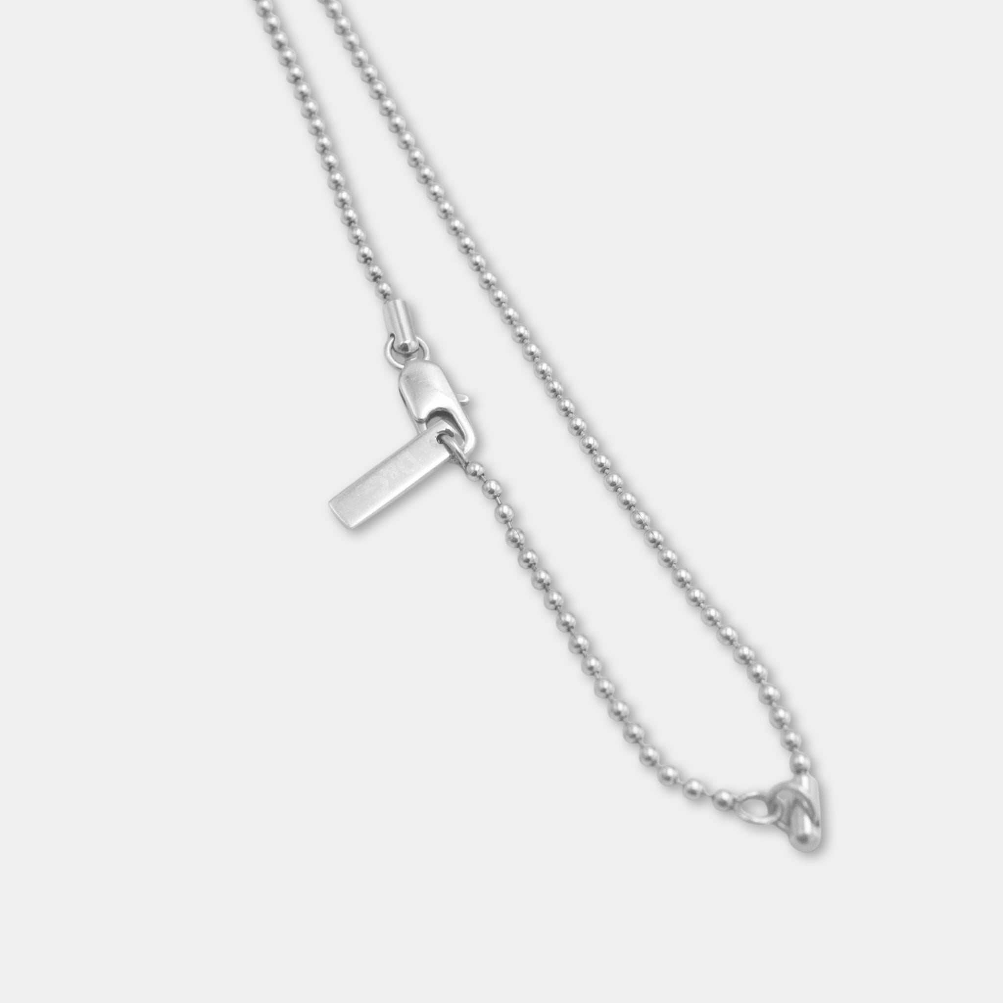 A silver necklace with a clasp and a small metal tag attached to it.