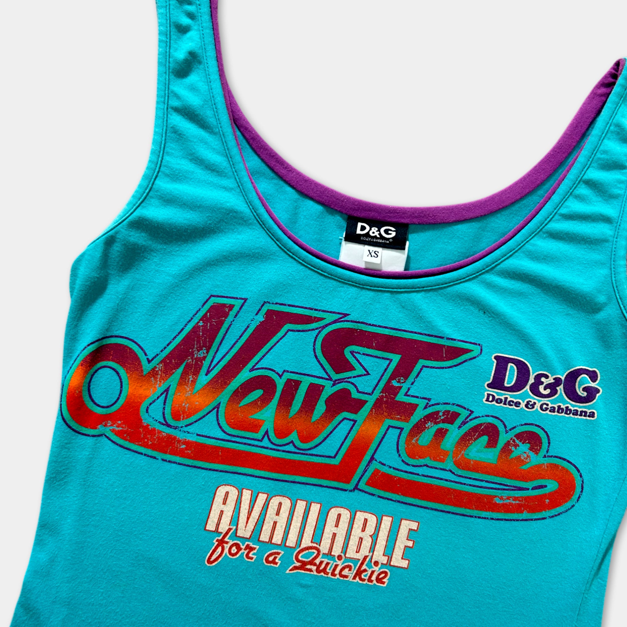 A turquoise tank top with a large graphic design on it, featuring the text "New Face" and "AVAILABLE for a Quickie" printed on it.