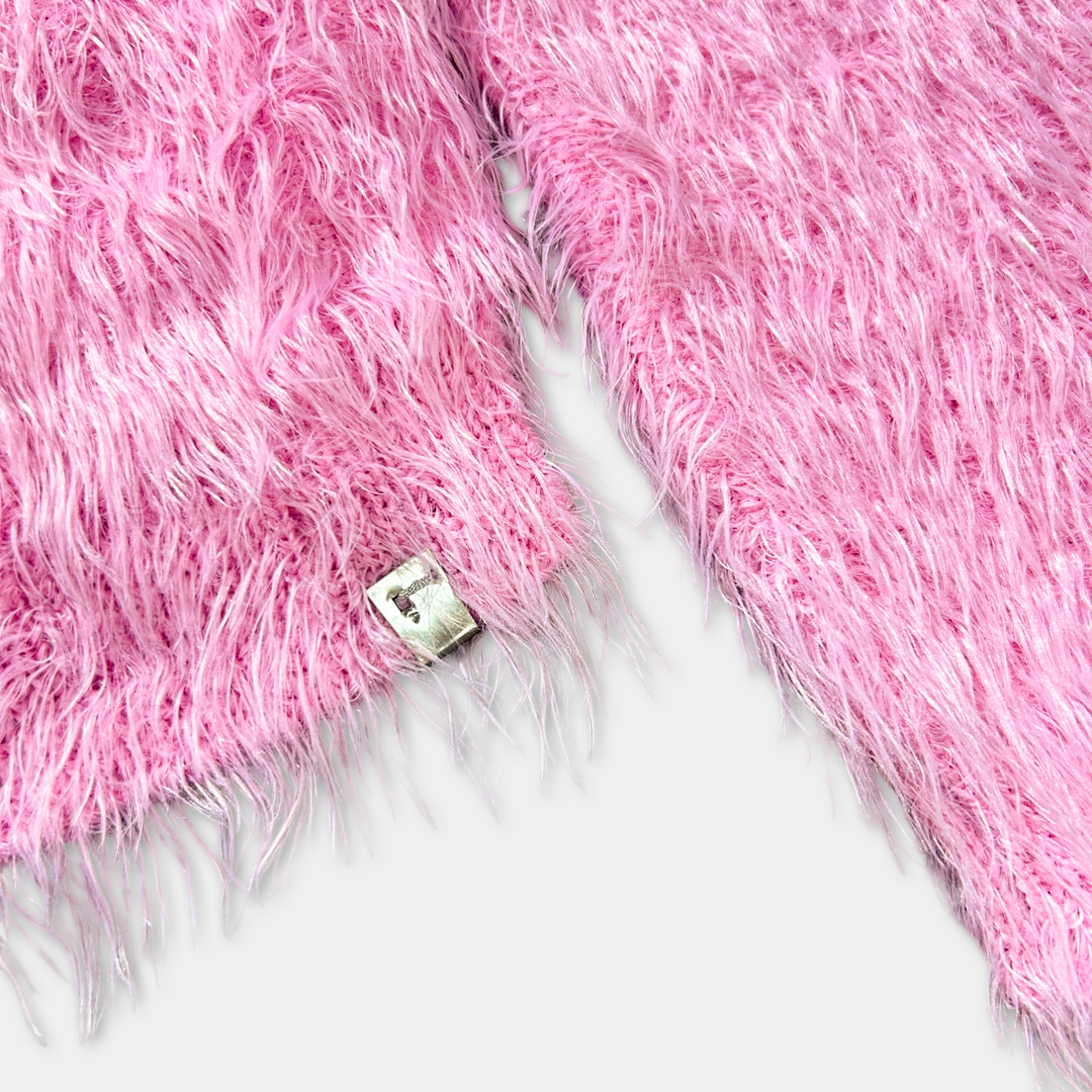 A close-up image of a pink fuzzy fabric with a small metal tag attached to it.