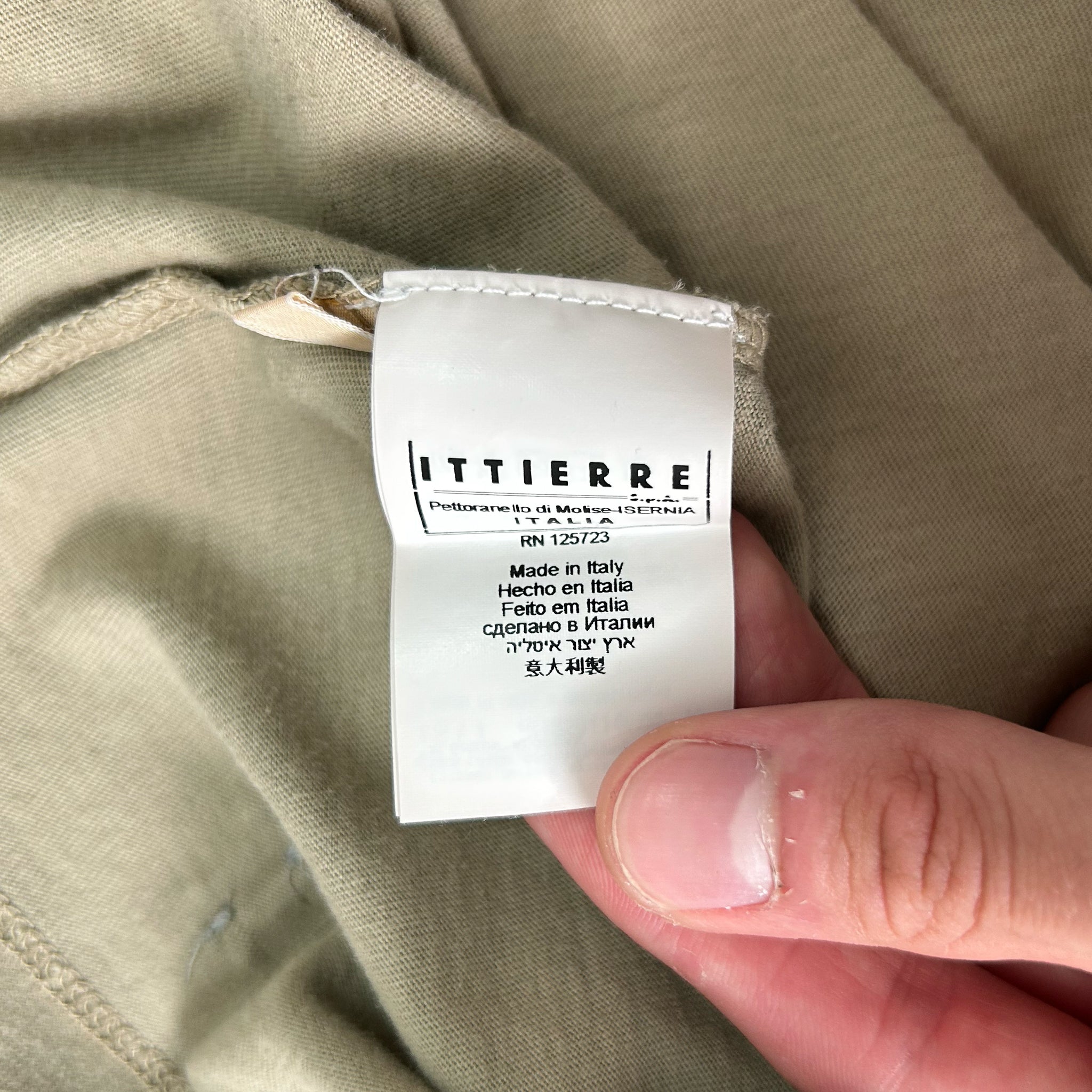 A hand holding a white label with text on it, against a beige background.