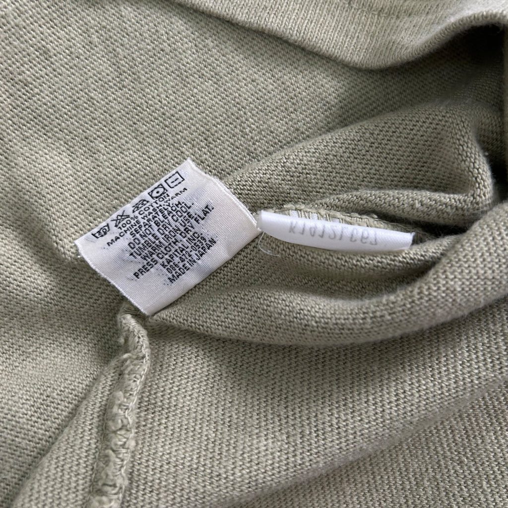 a close-up view of a grey fabric, possibly a sweater or a shirt, with a white label attached to it. The label appears to contain text and symbols, but the image does not contain any text that can be transcribed in less than 500 characters.