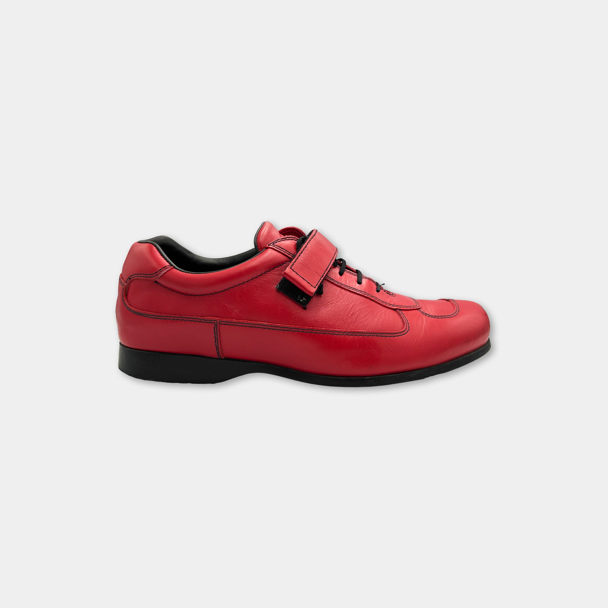 A red leather shoe with a black sole and strap is shown against a white background.