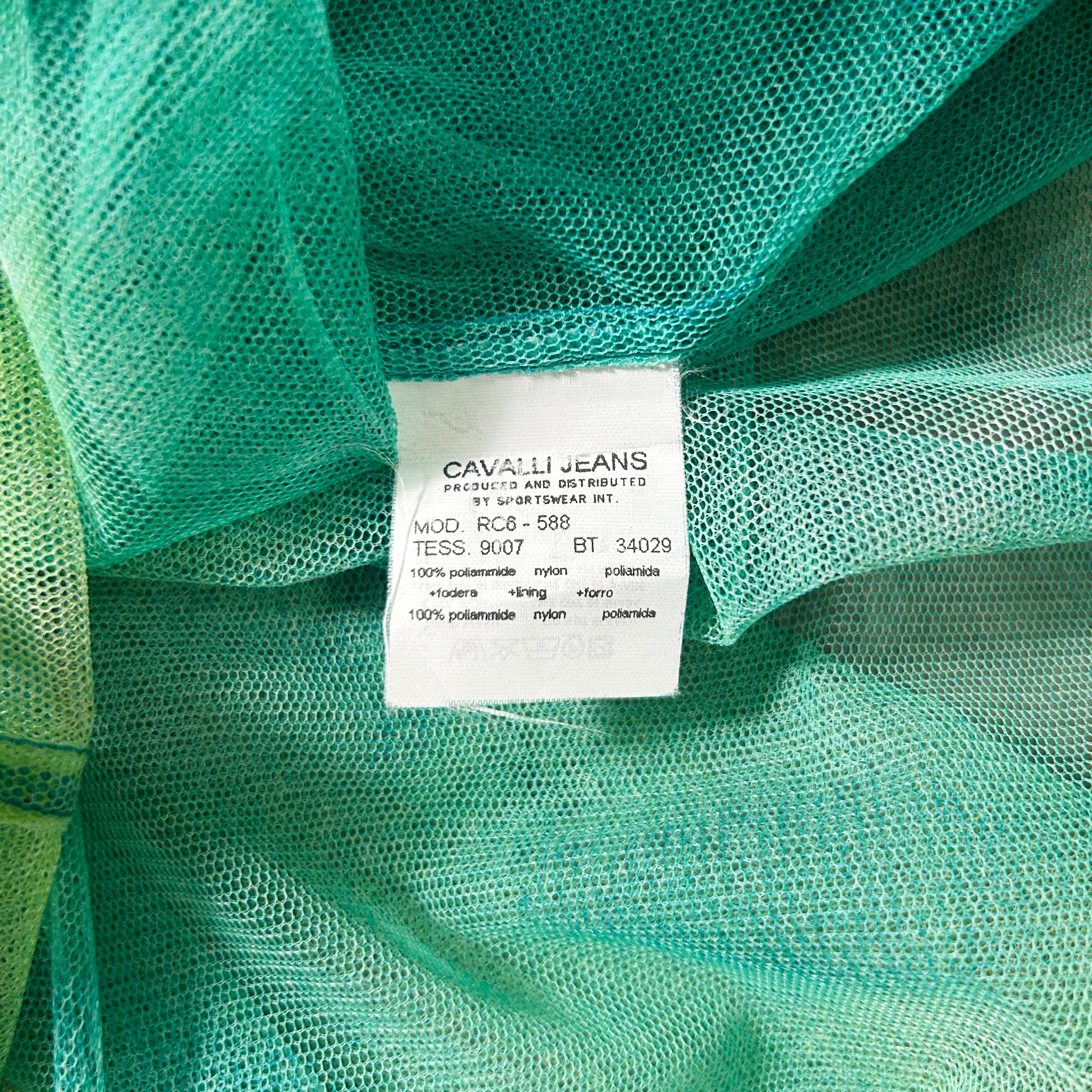 a close-up view of a green mesh fabric, with a label attached to it. The label appears to be a product label from a clothing brand, providing information about the fabric and its properties.