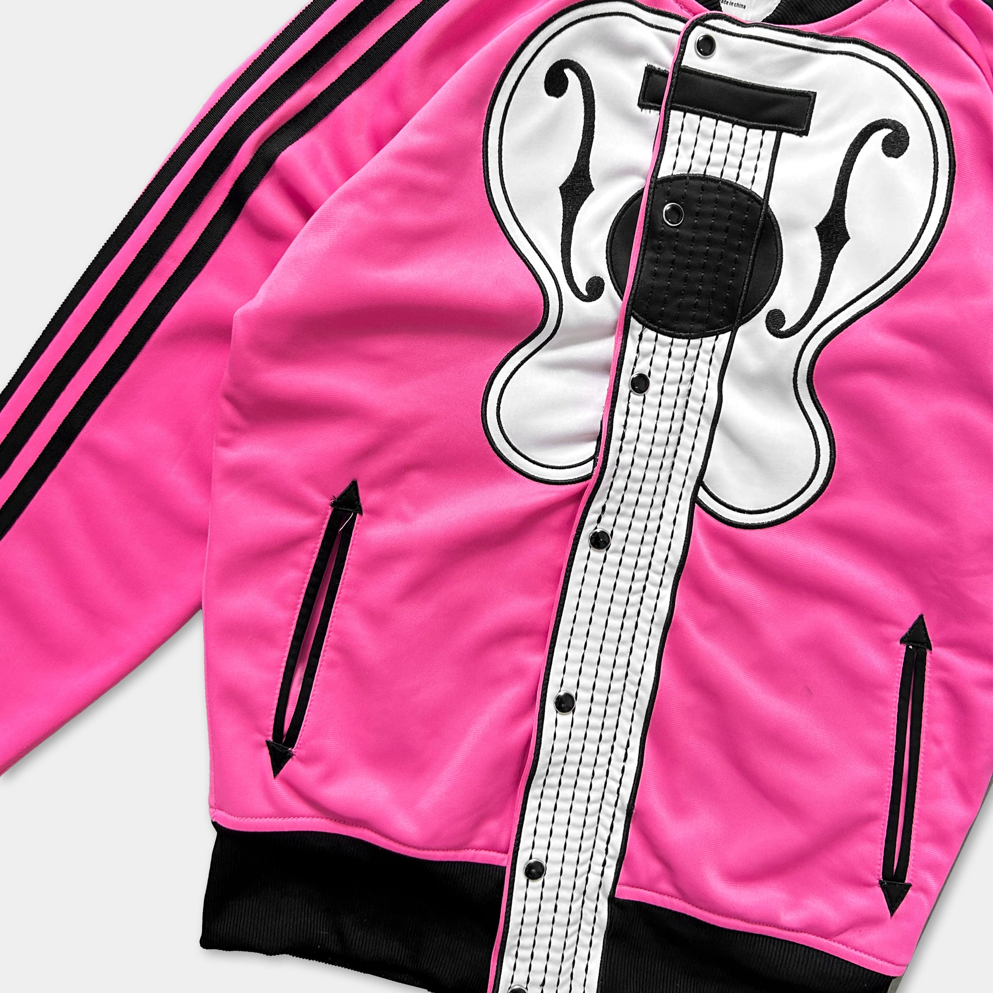 A bright pink track jacket with a black and white guitar design on the front.