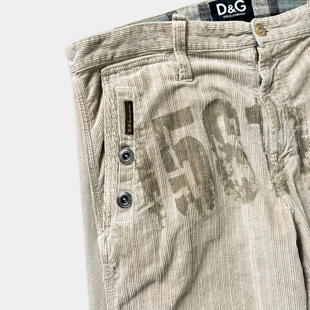 A pair of beige corduroy pants with a large "D&G" logo printed on the front pocket area.
