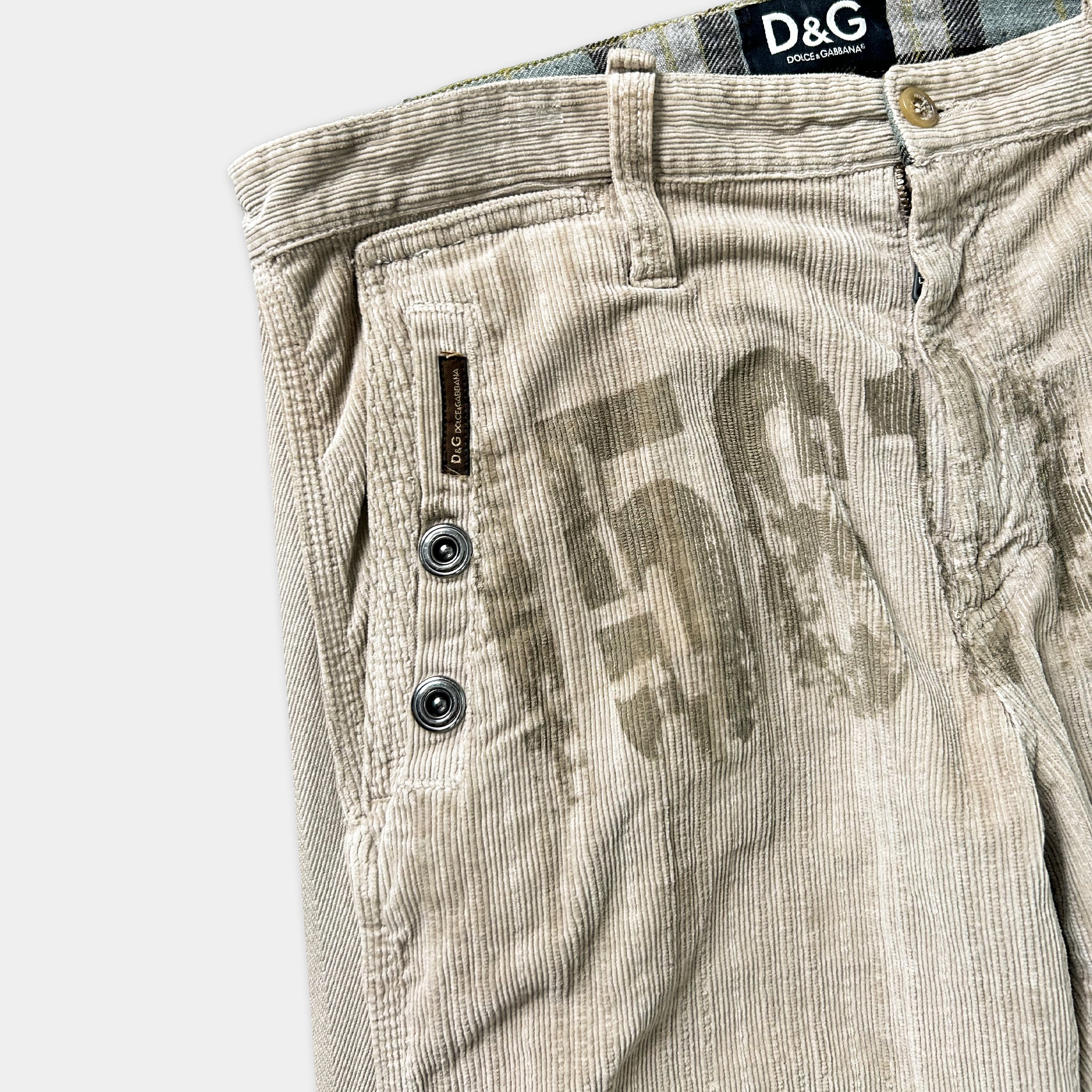A pair of beige corduroy pants with a large "D&G" logo printed on the front pocket area.